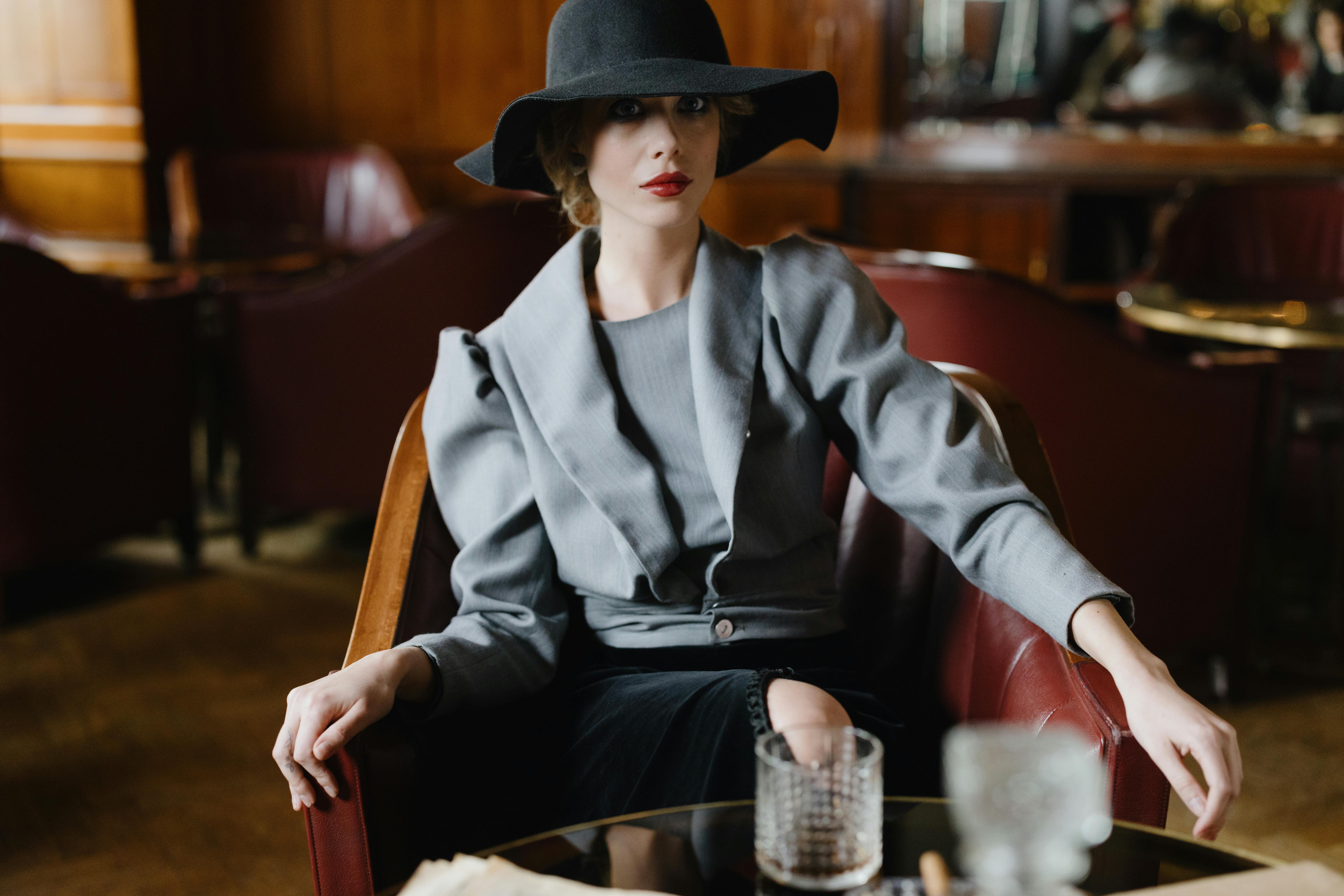 A person in a hat and gray suit sits in a leather chair.