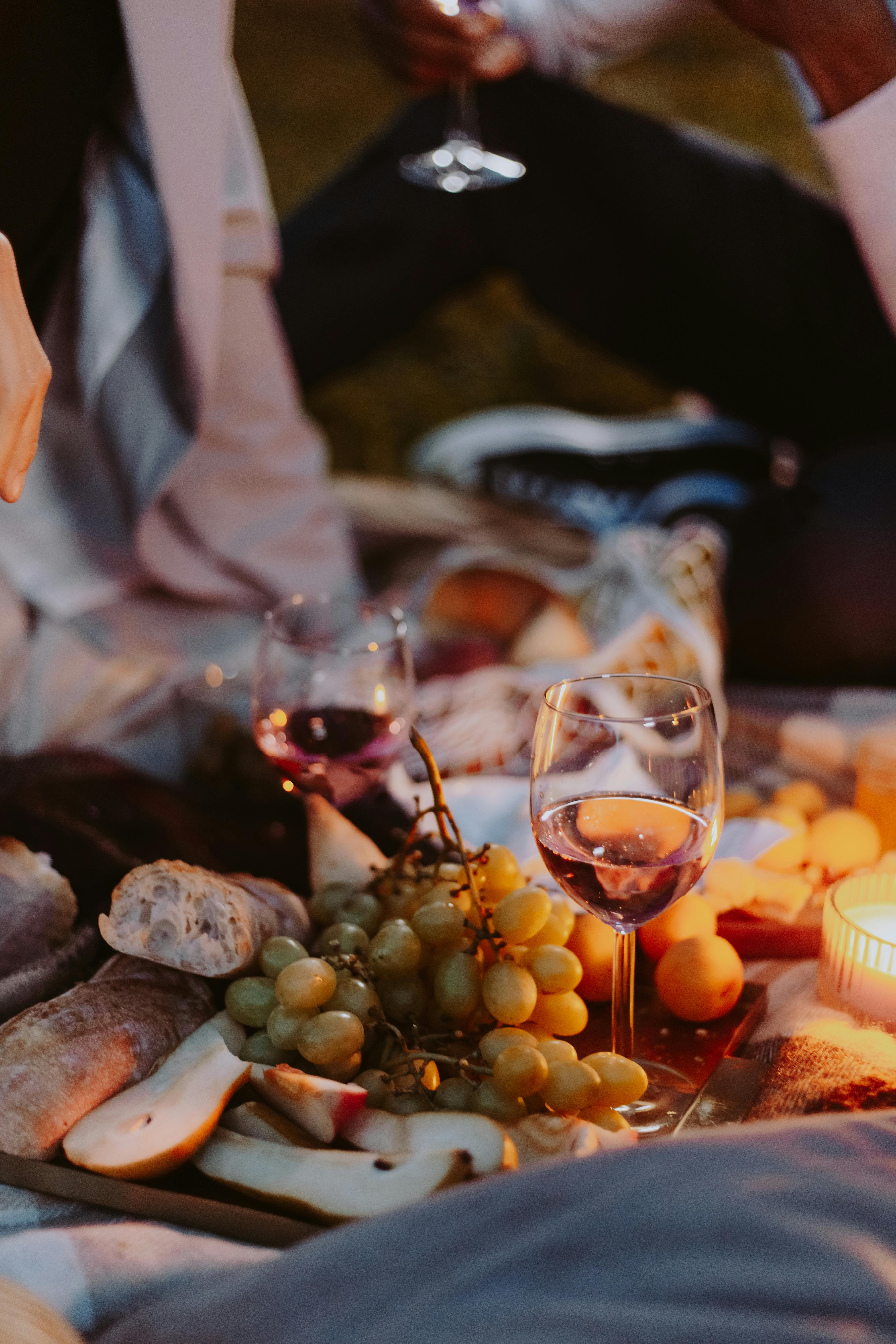 Picnic scene with wine, grapes, bread, candle, and people.