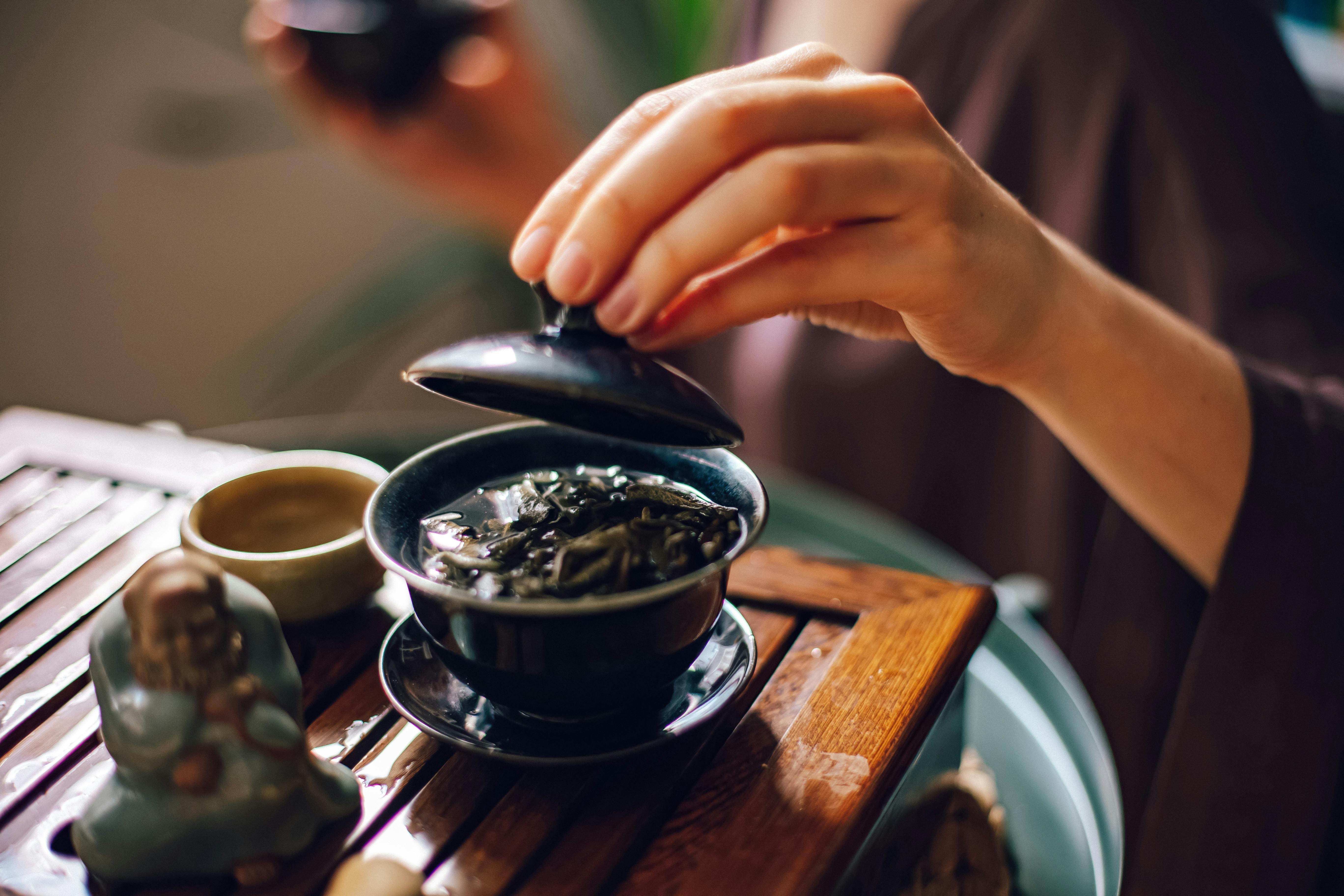A person prepares tea with a small figurine on a wooden tray.