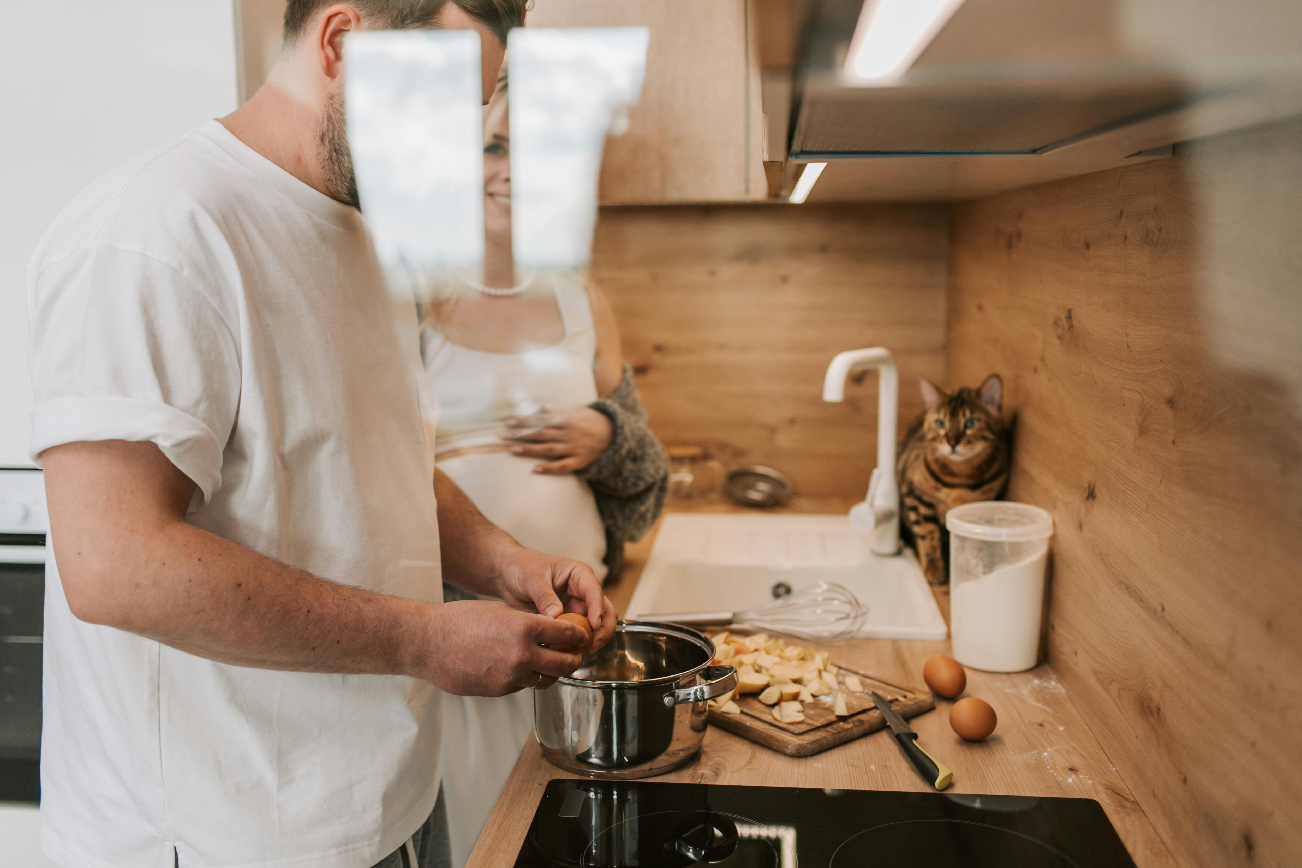 Two people cooking in kitchen, cat sitting by the sink.
