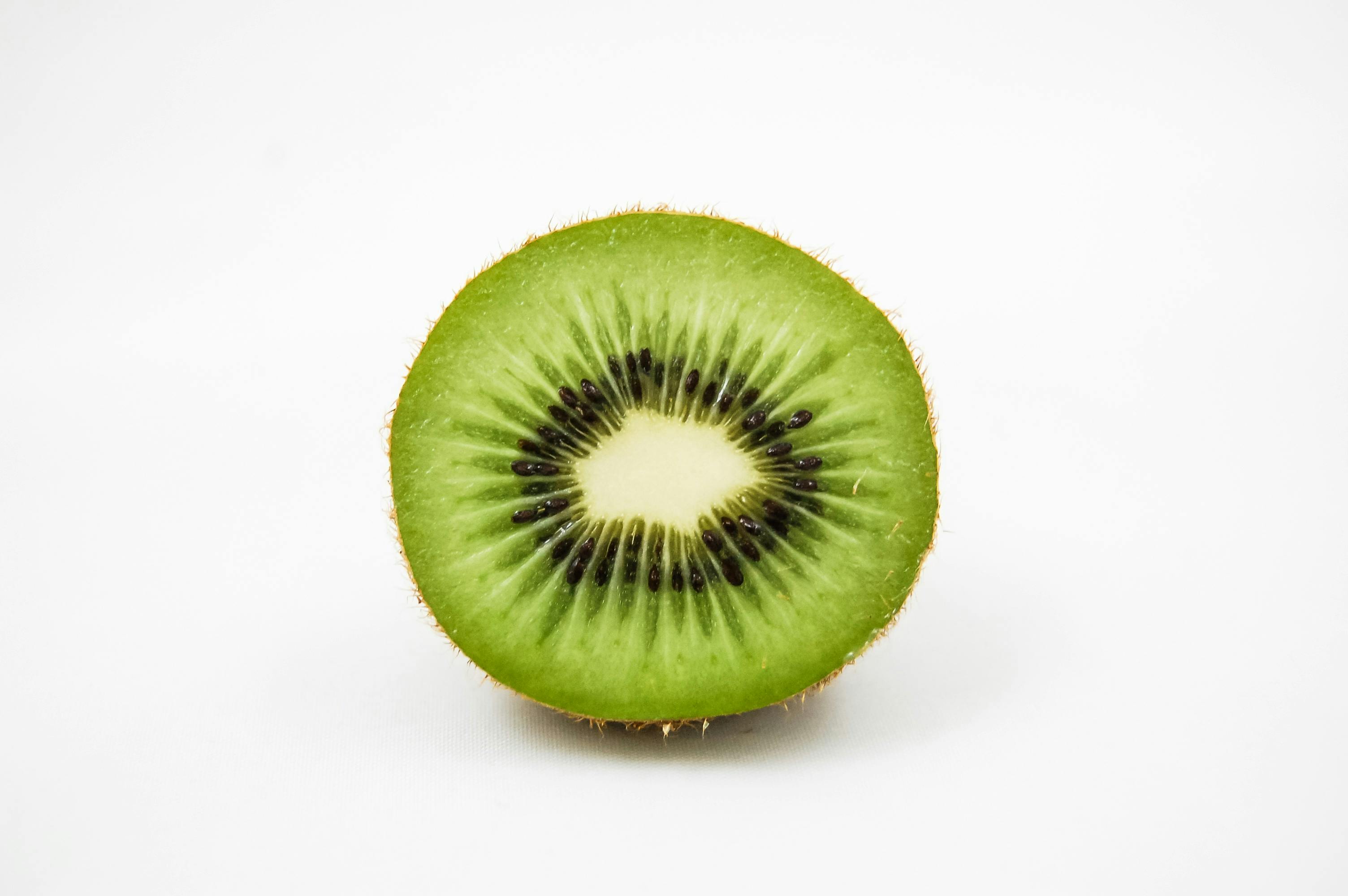 A sliced kiwi fruit on a white background, seeds visible.