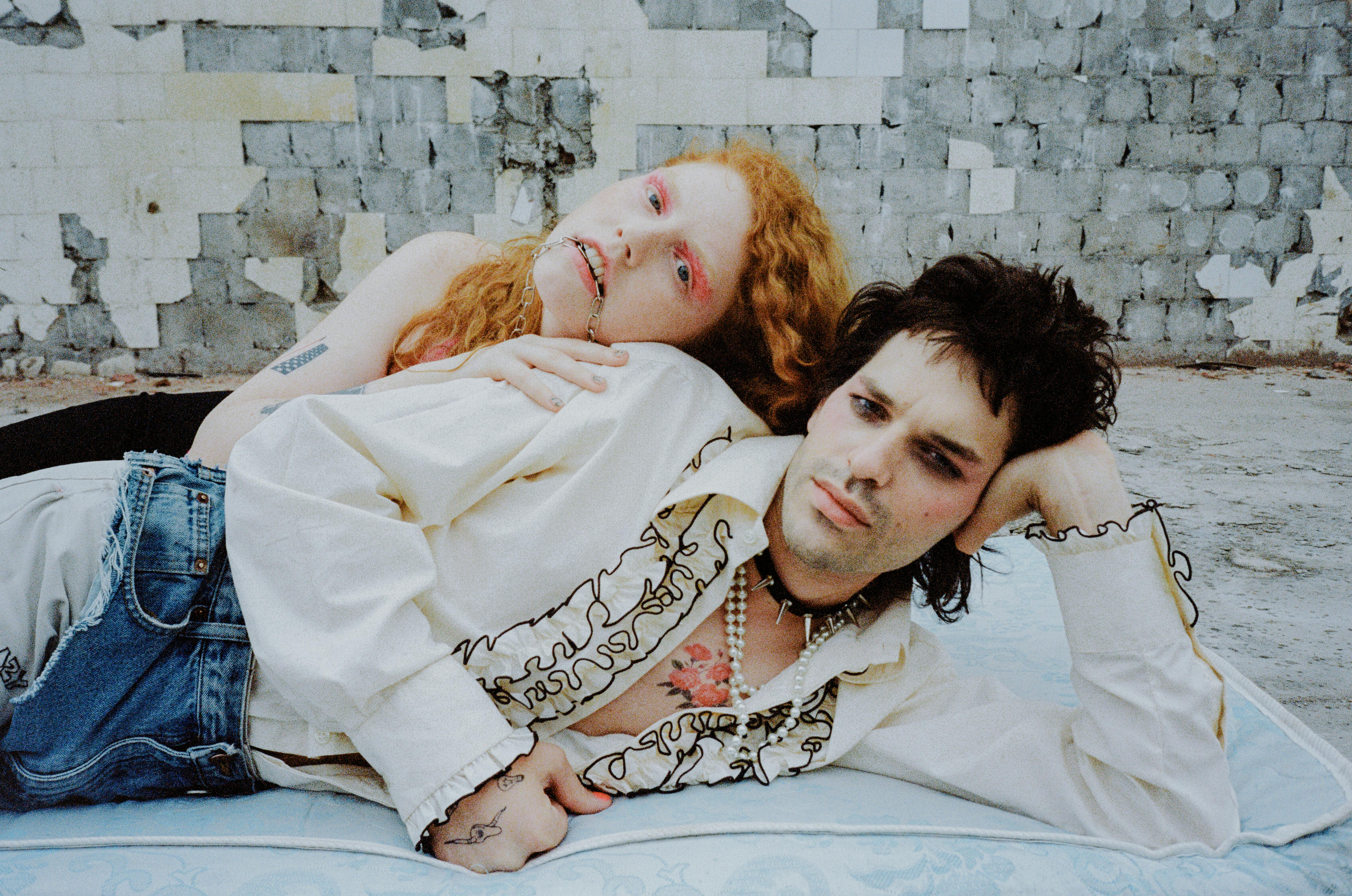Two people with dramatic makeup lying down against a brick wall.
