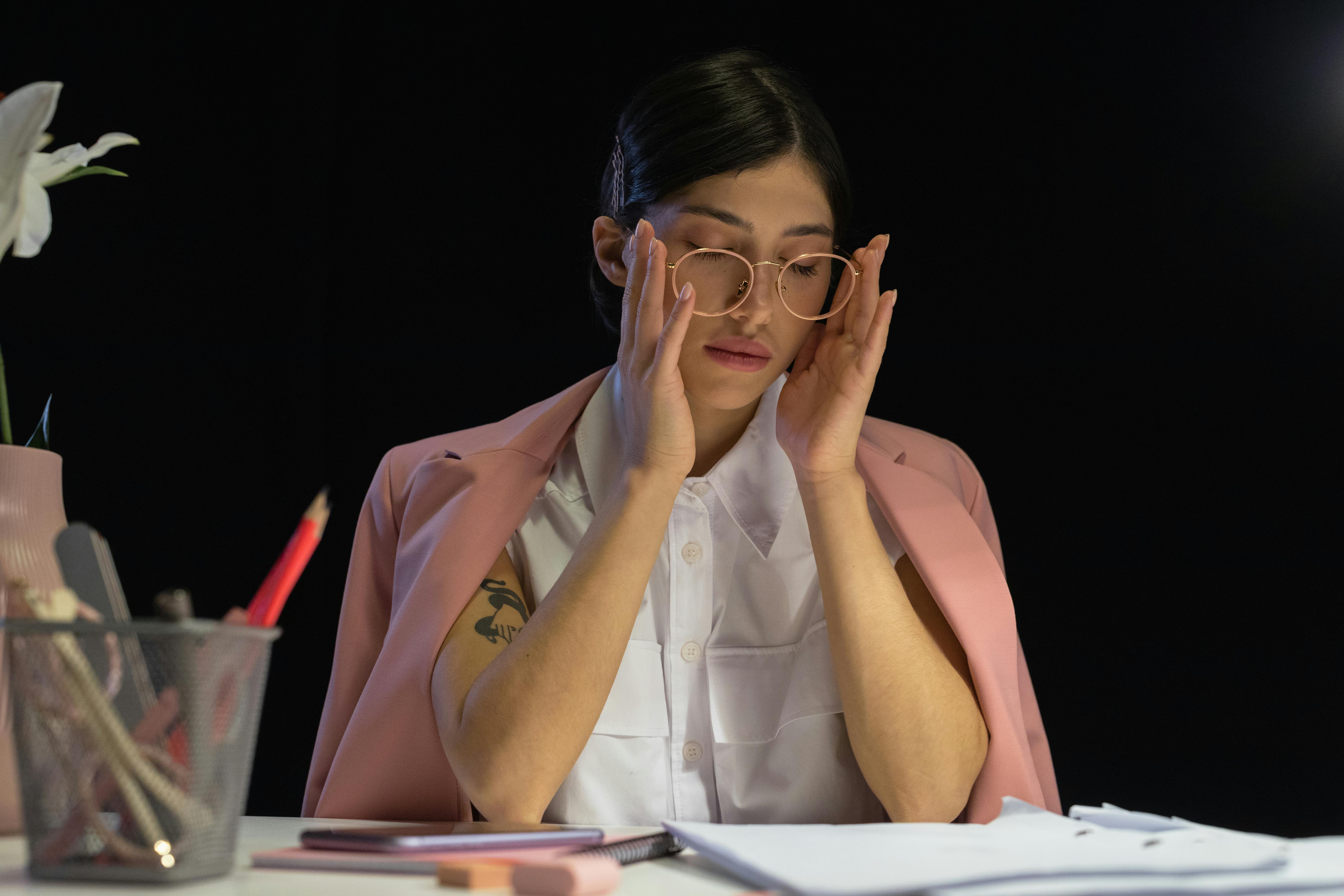 Person with glasses rubbing temples at a desk with papers.