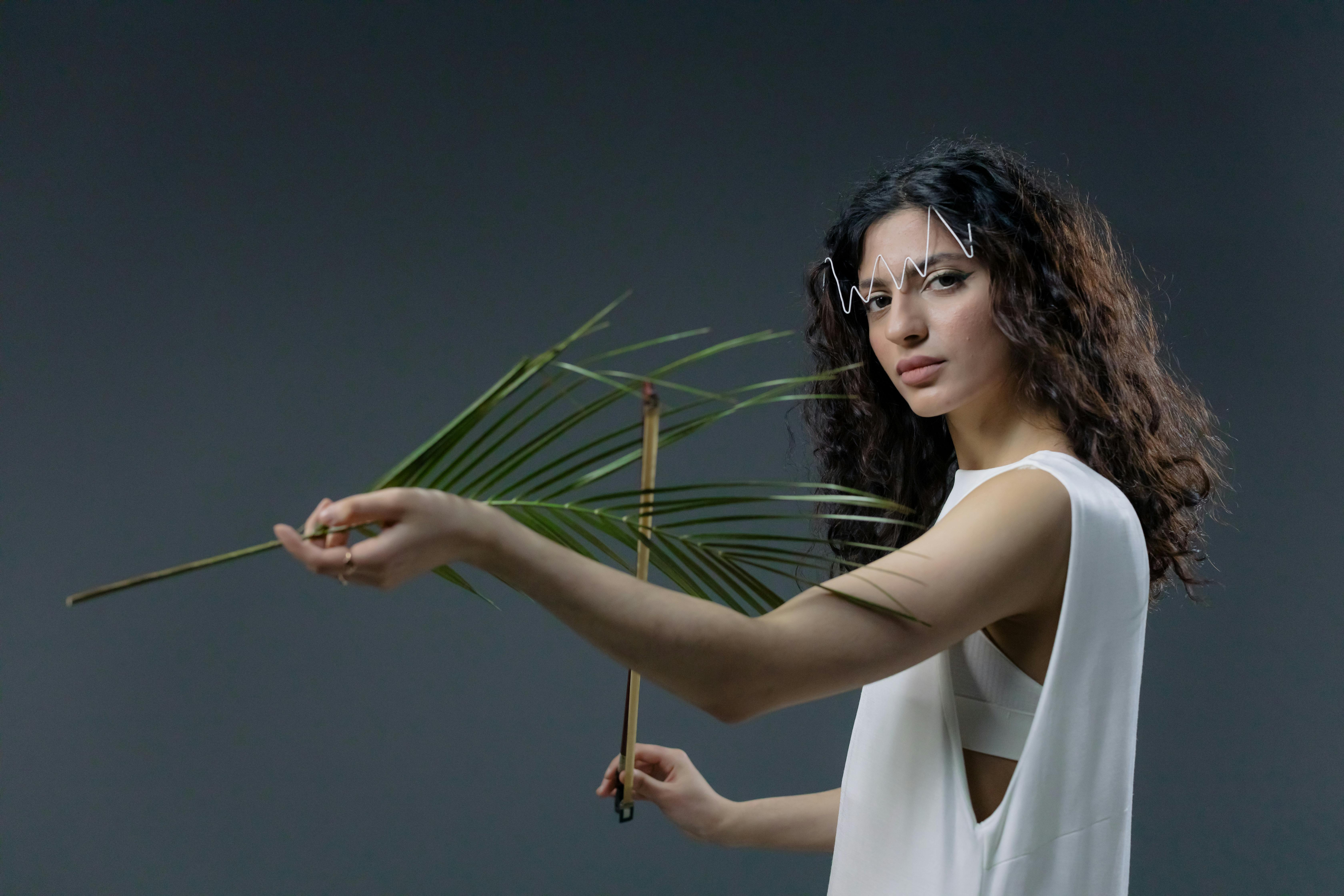 Person holding palm leaf, wearing white outfit, creative makeup.