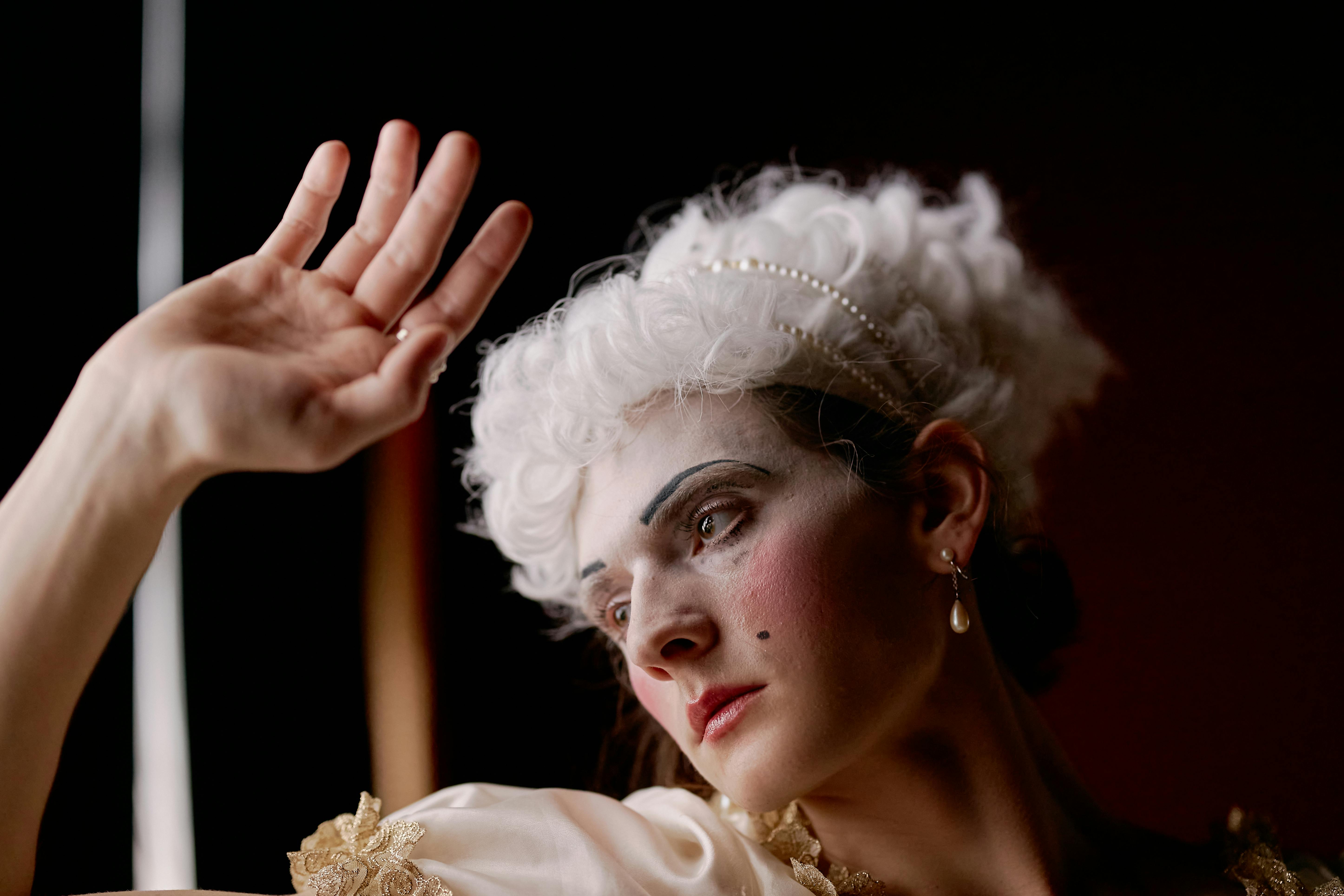 Person in historical costume with white wig, dramatic makeup, posing.