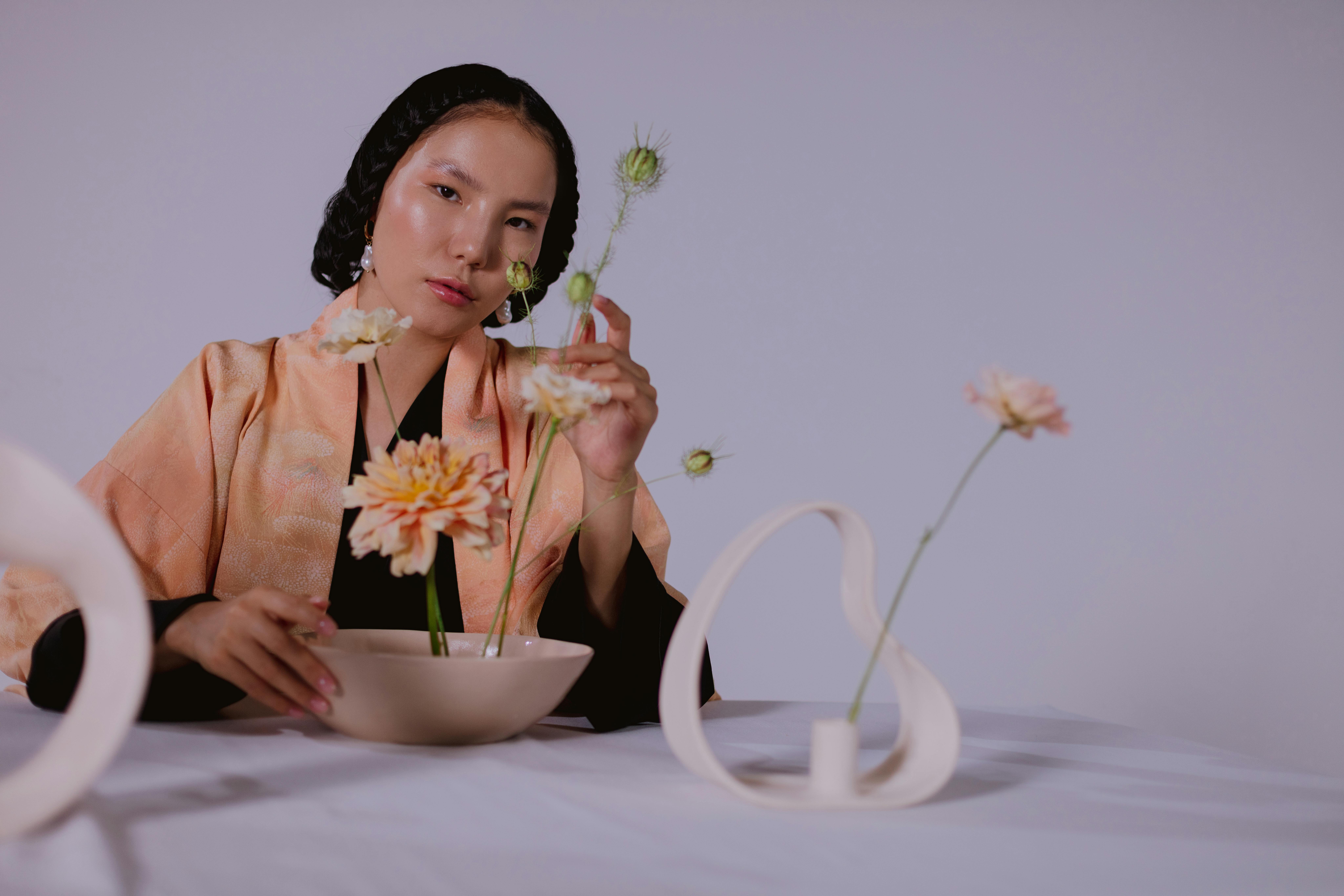 A person arranges flowers in a bowl with a minimalist vase.