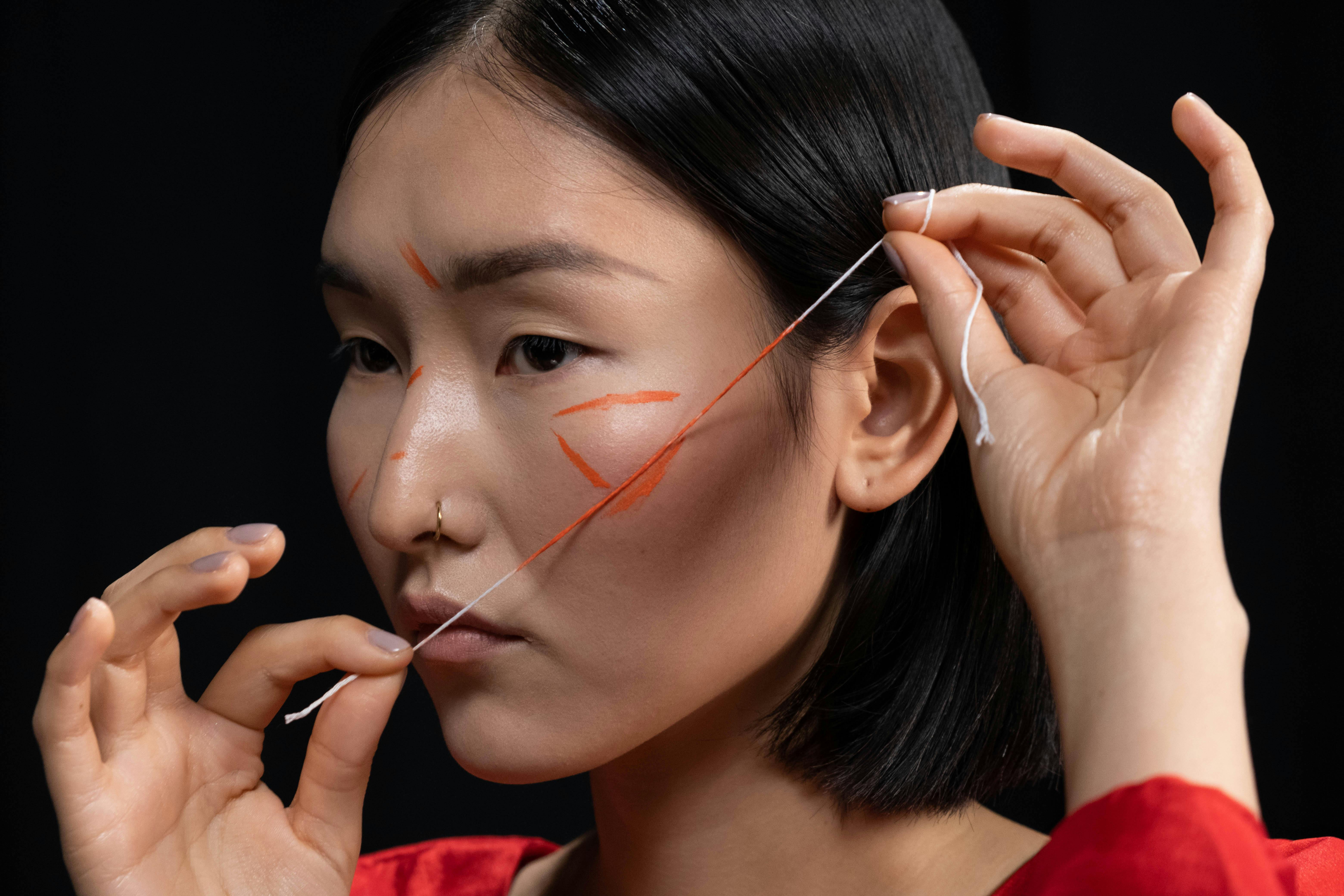 Person with face paint holding string near face, black background.