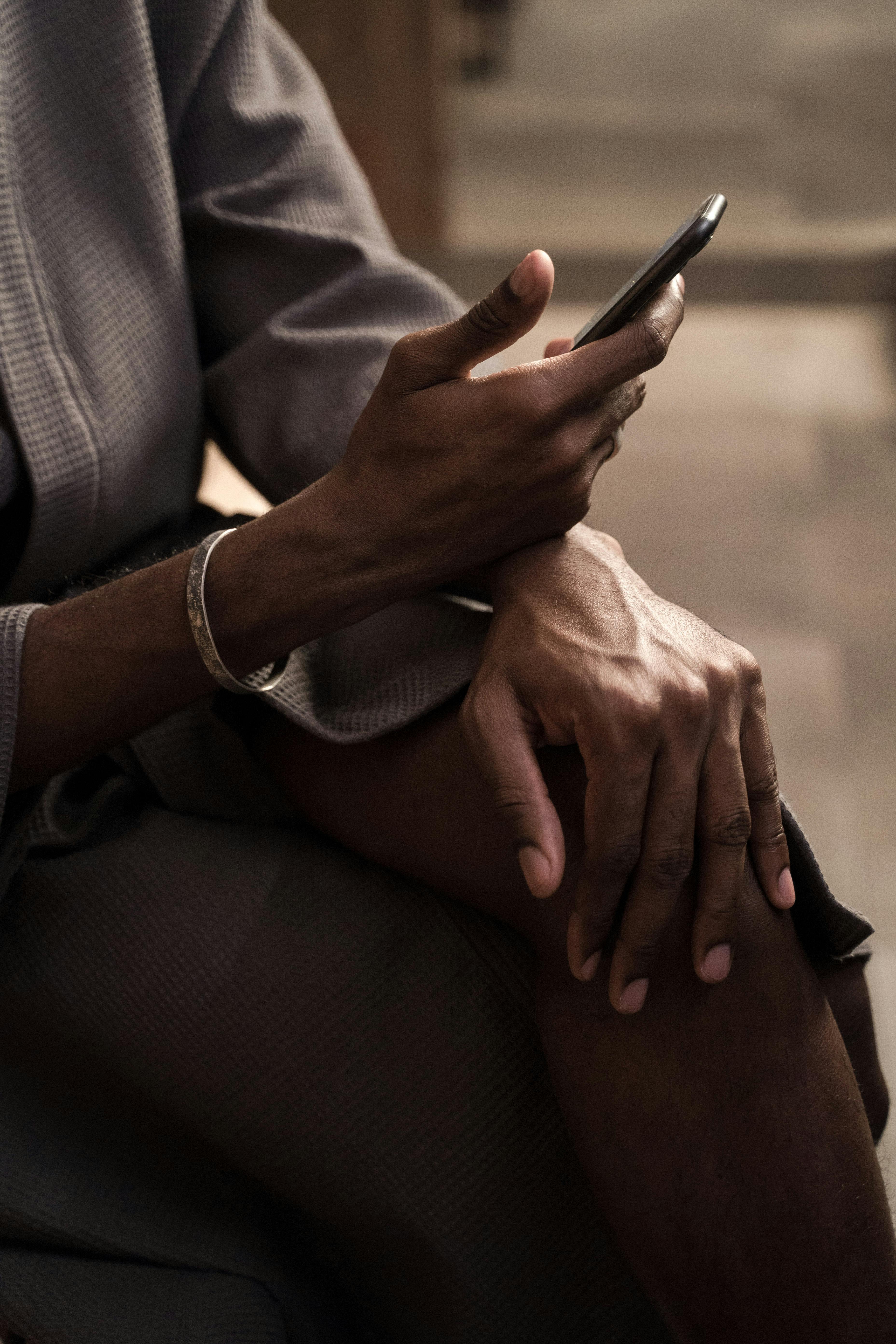 Person sitting, holding a smartphone, wearing a robe and bracelet.