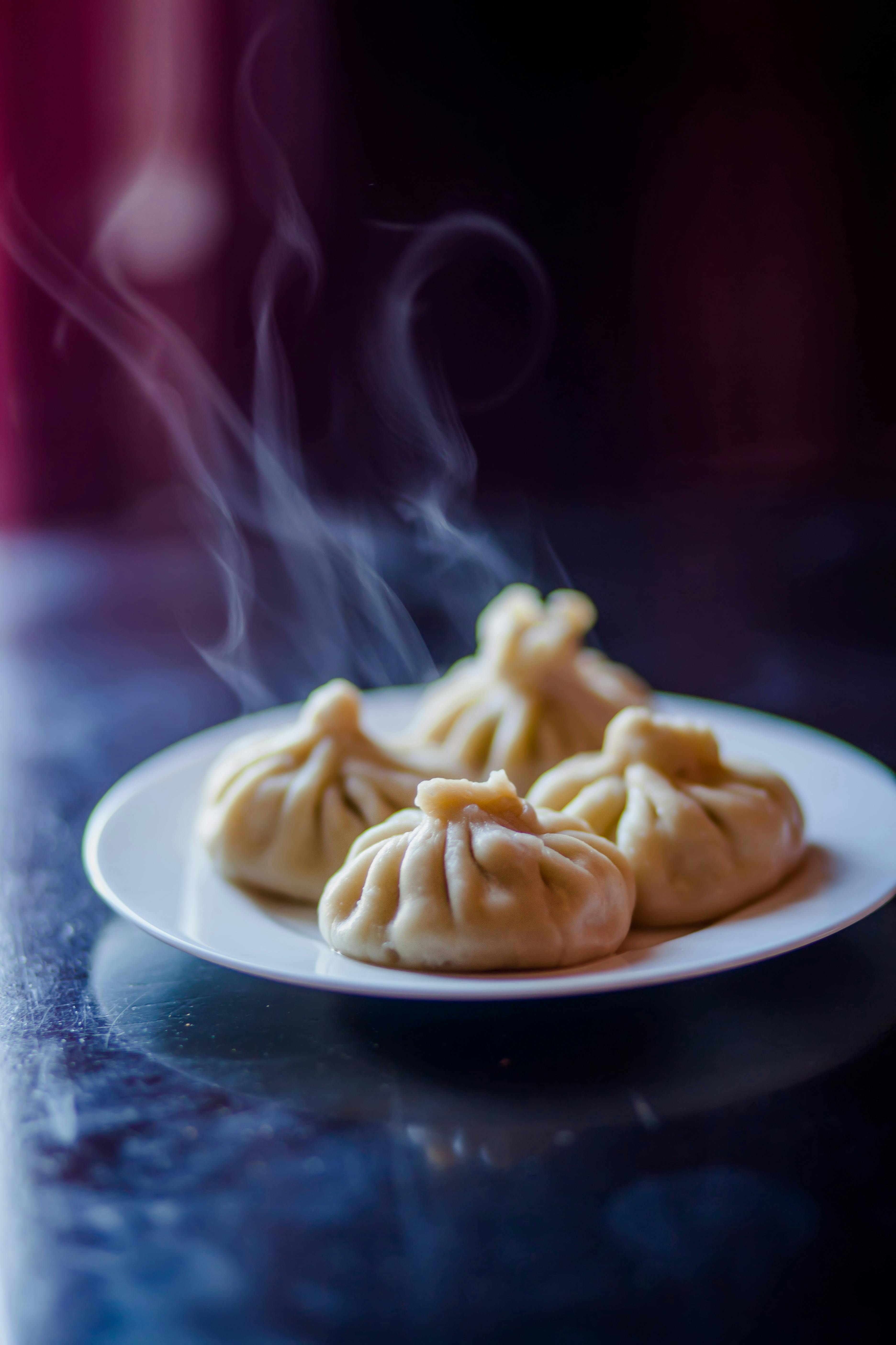 Steaming dumplings on a white plate, dark background, appetizing.