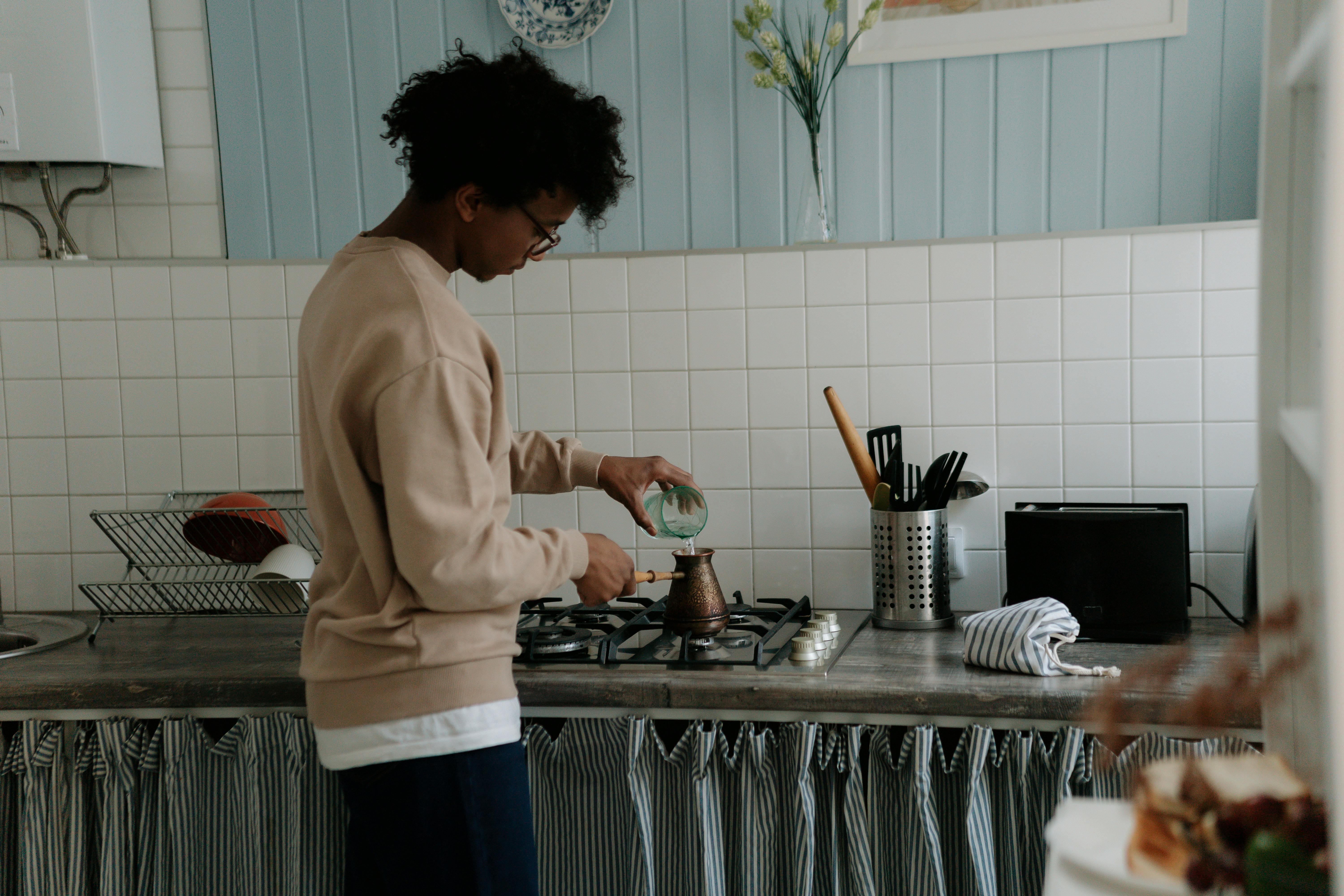 Person pouring water into a pot on a kitchen stove.