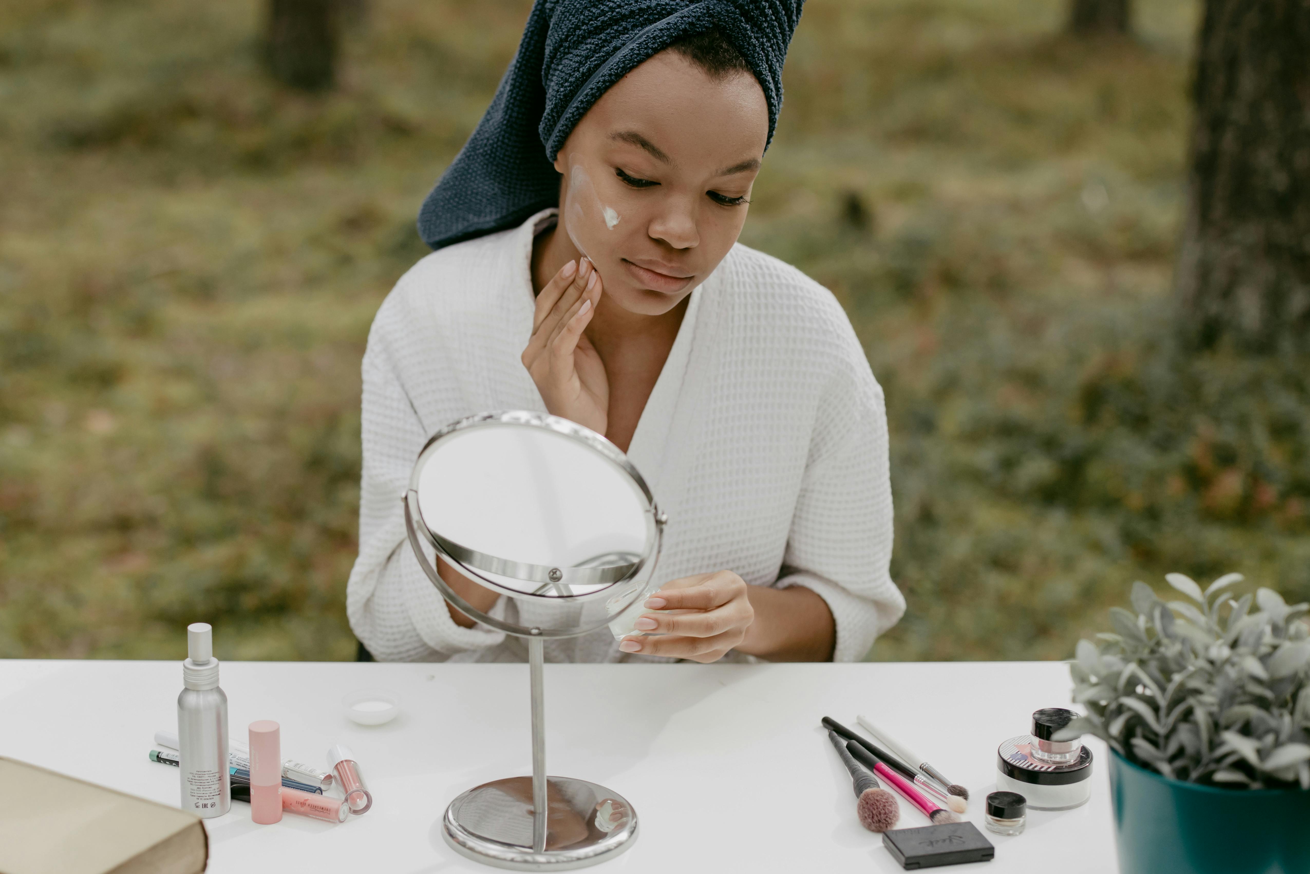 Person applying skincare at a table with beauty products outdoors.