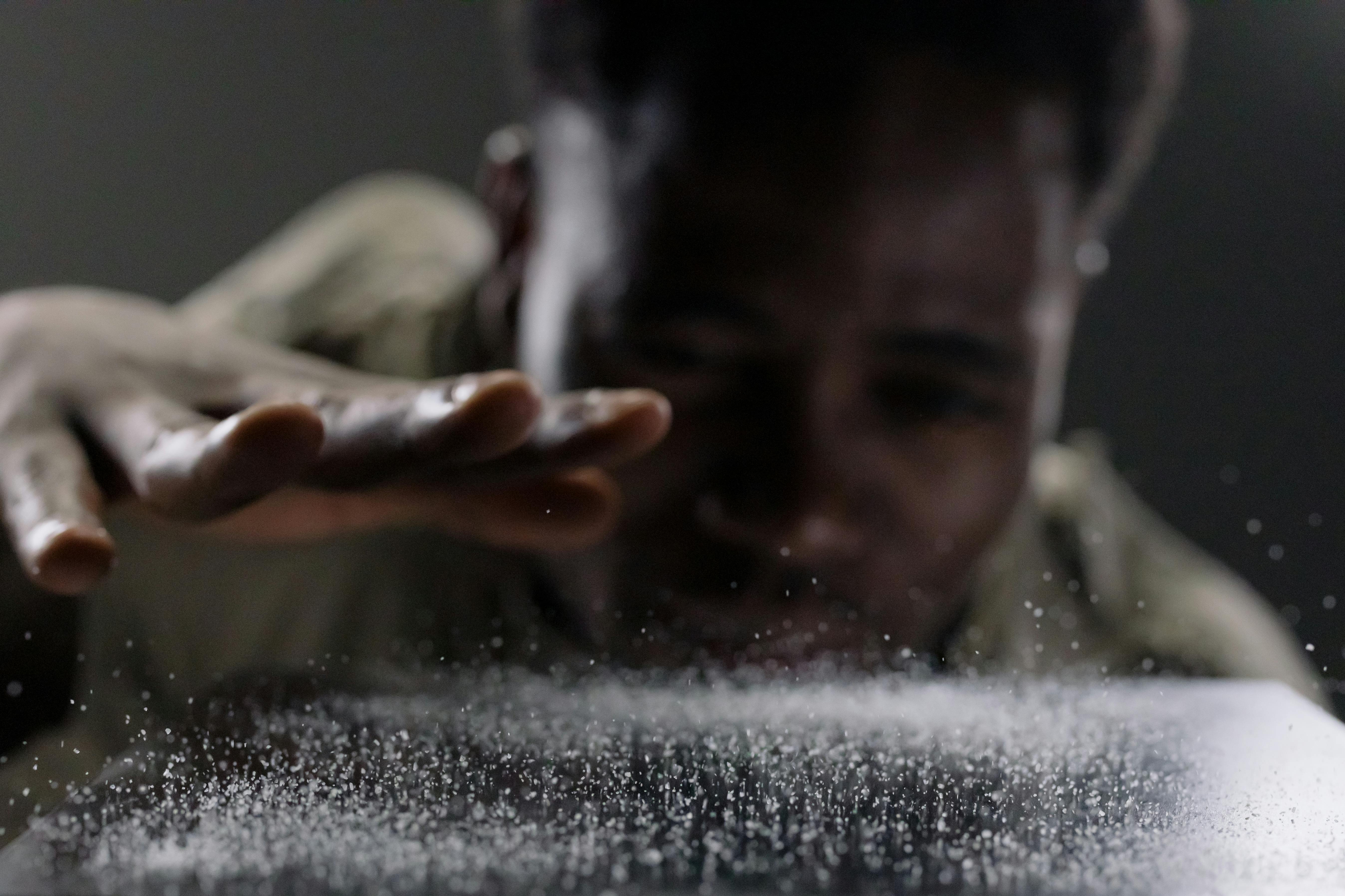 Person blowing on surface, causing particles to scatter dramatically.