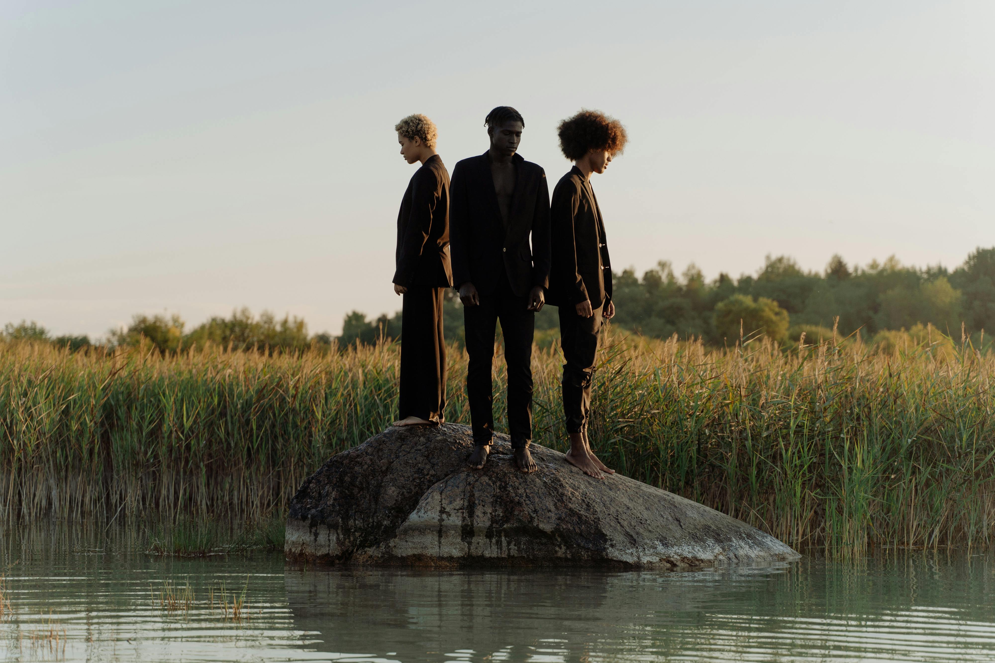 Three people stand on a rock in the water.