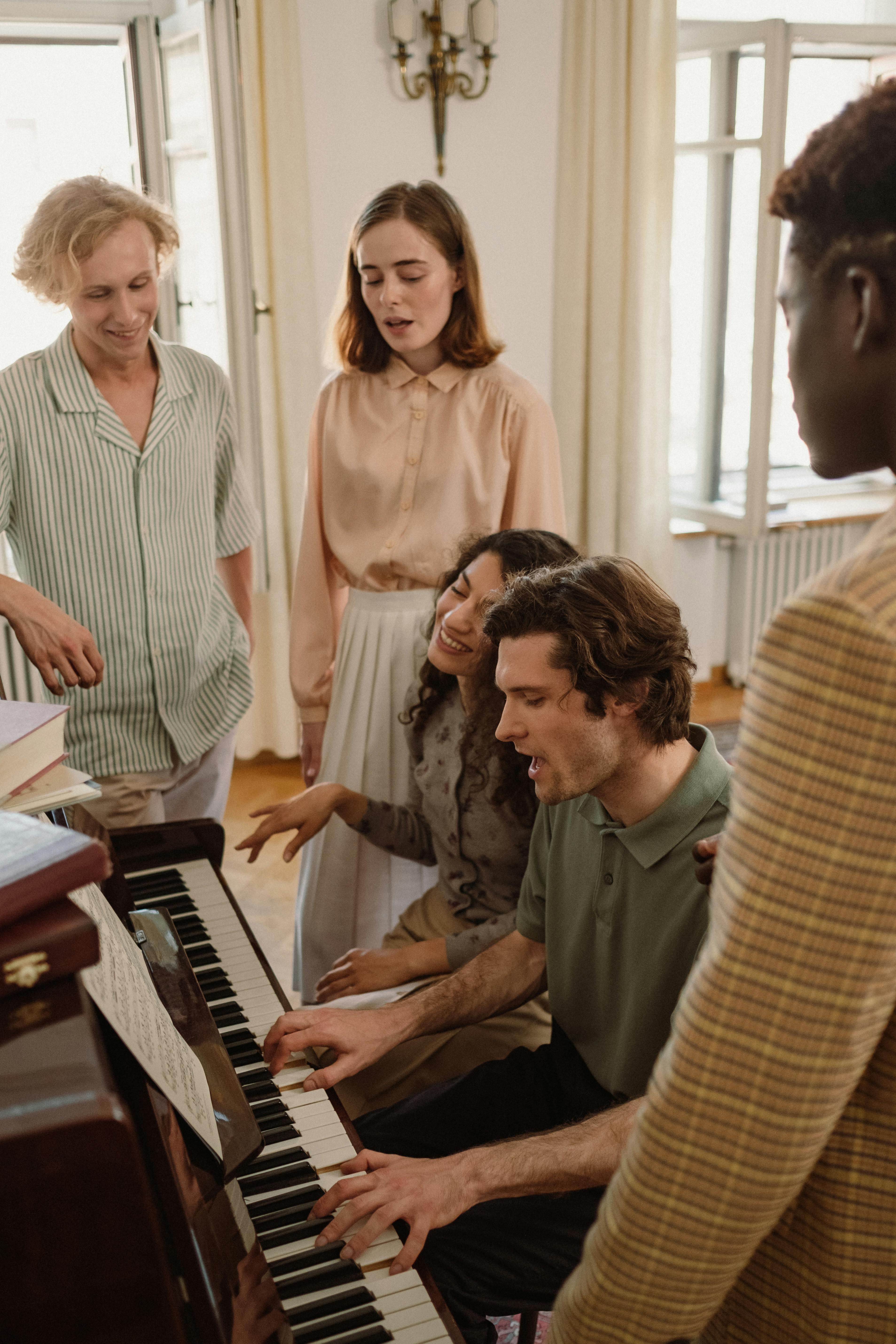 Group of people gathered around piano, singing and playing music.