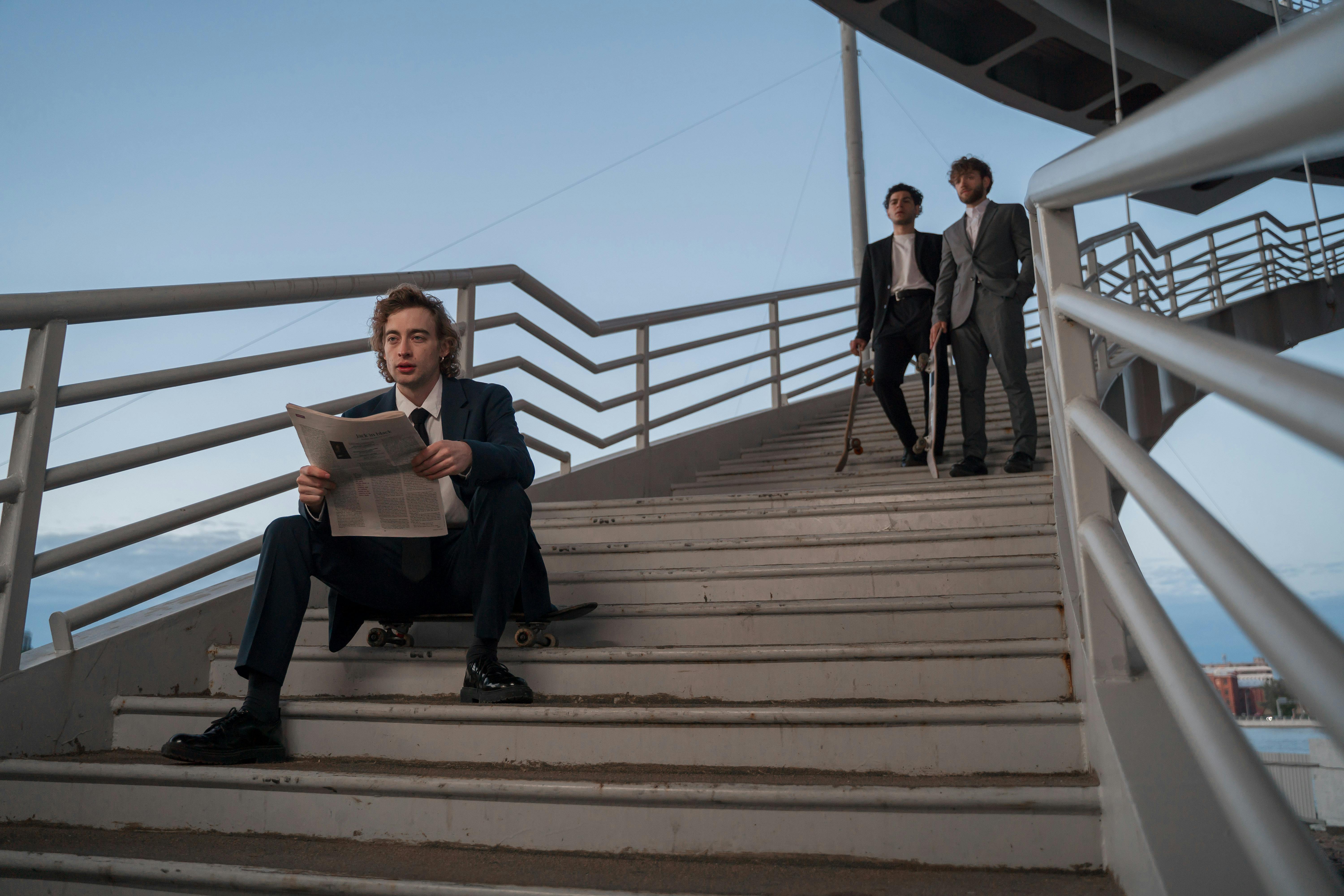 Men in suits on stairs with skateboards and a newspaper.