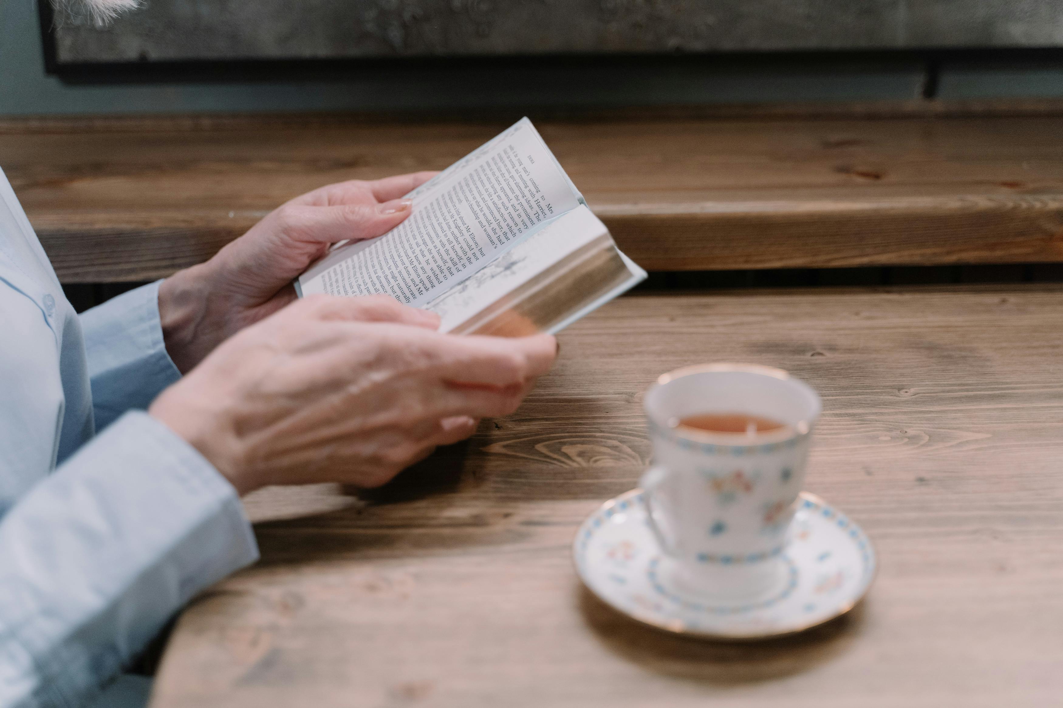 Person reading a book with a cup of tea nearby.