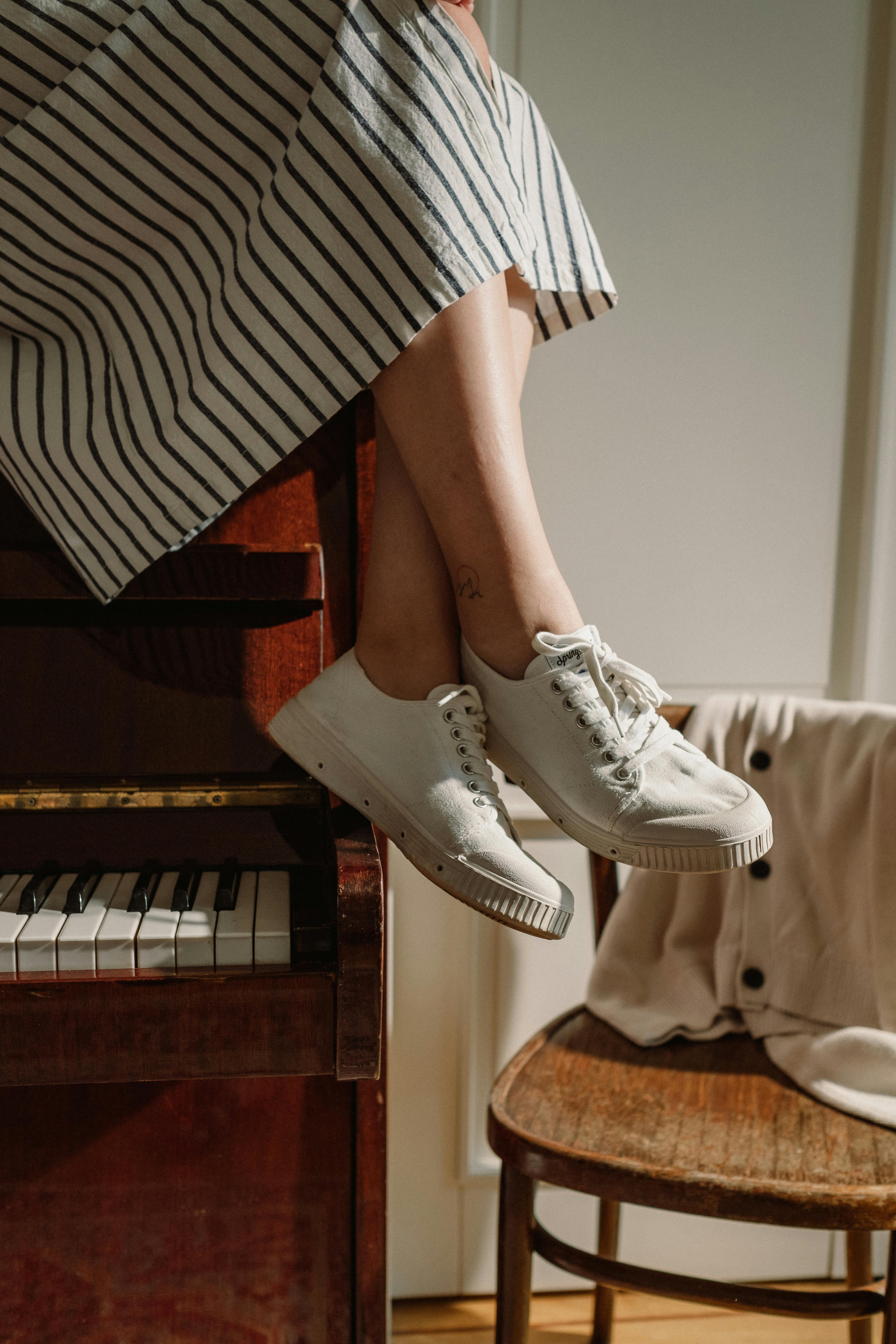 Person in striped dress sitting on piano, wearing white sneakers.