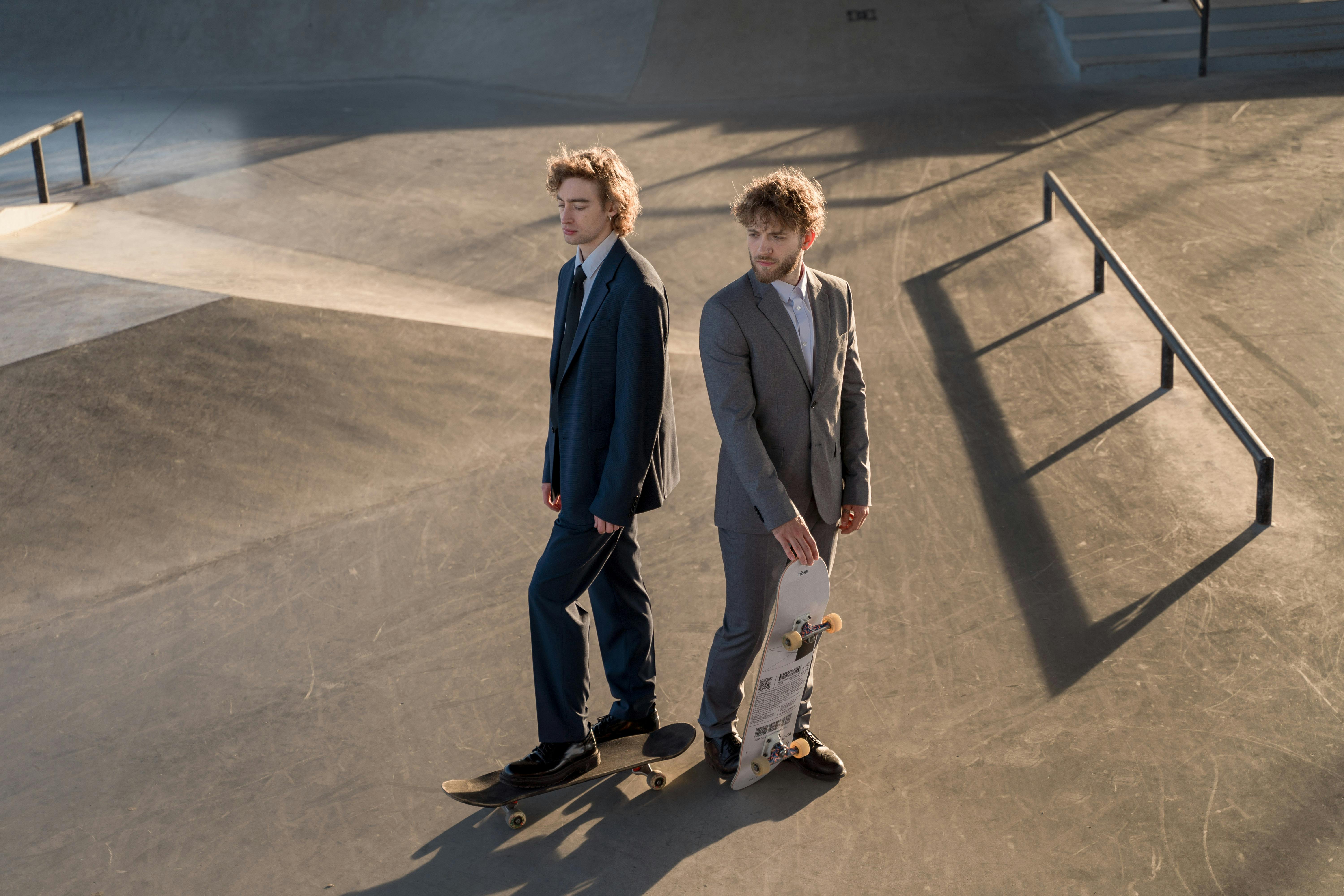 Two people in suits with skateboards at a skatepark.