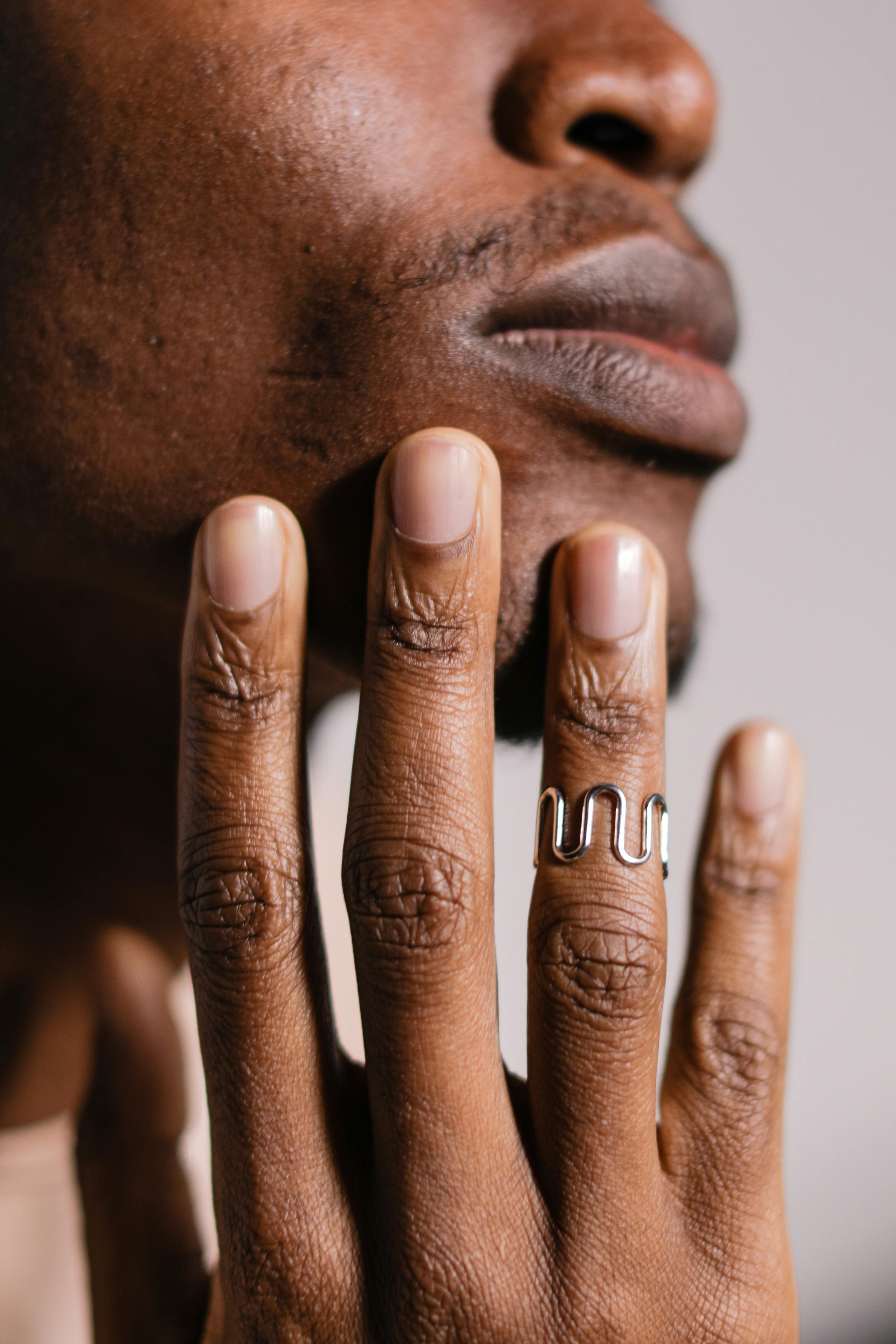 Hand with wavy silver ring touches face, close-up view.