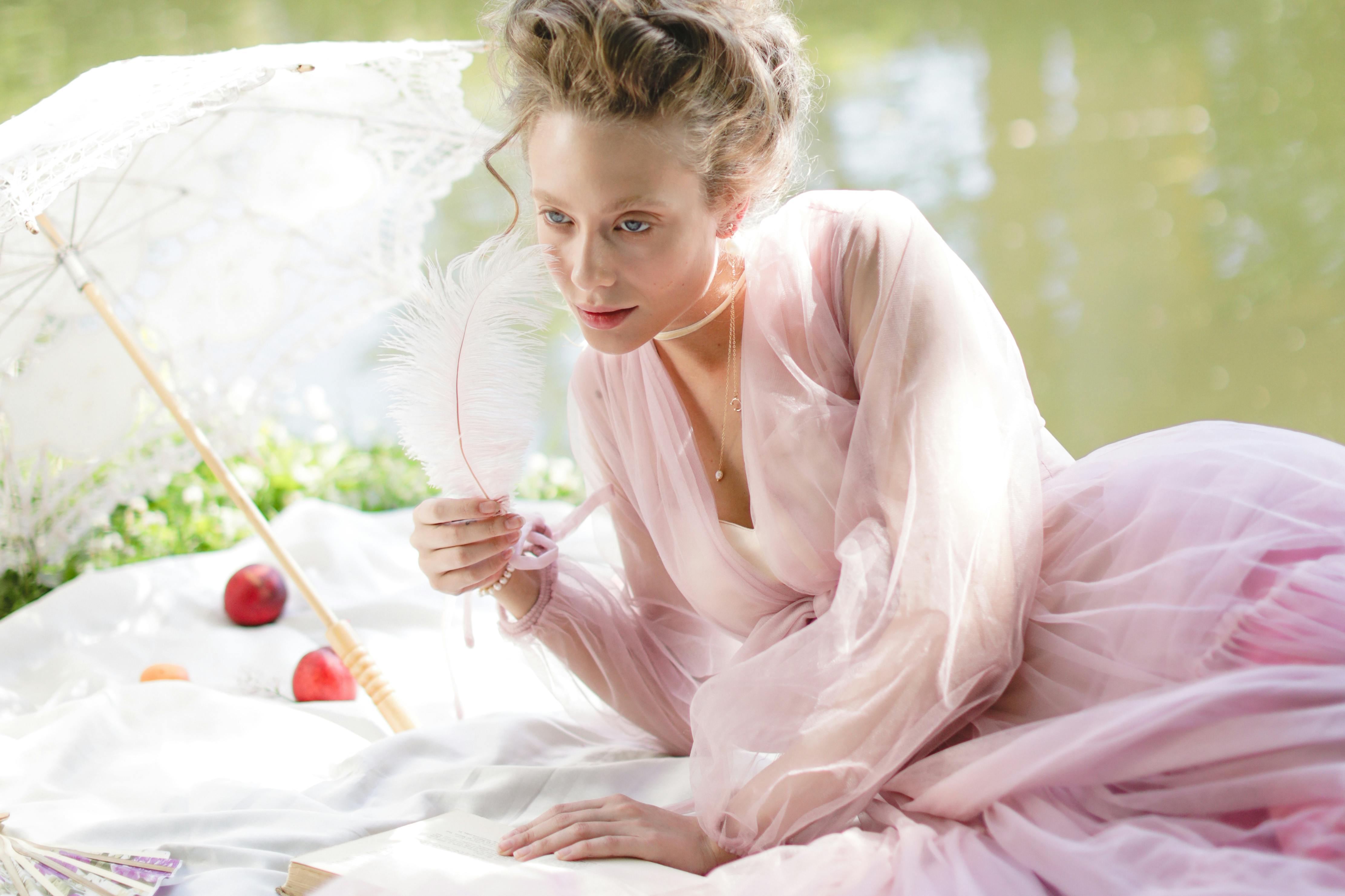 A person in a pink dress holds a feather near a book and umbrella.
