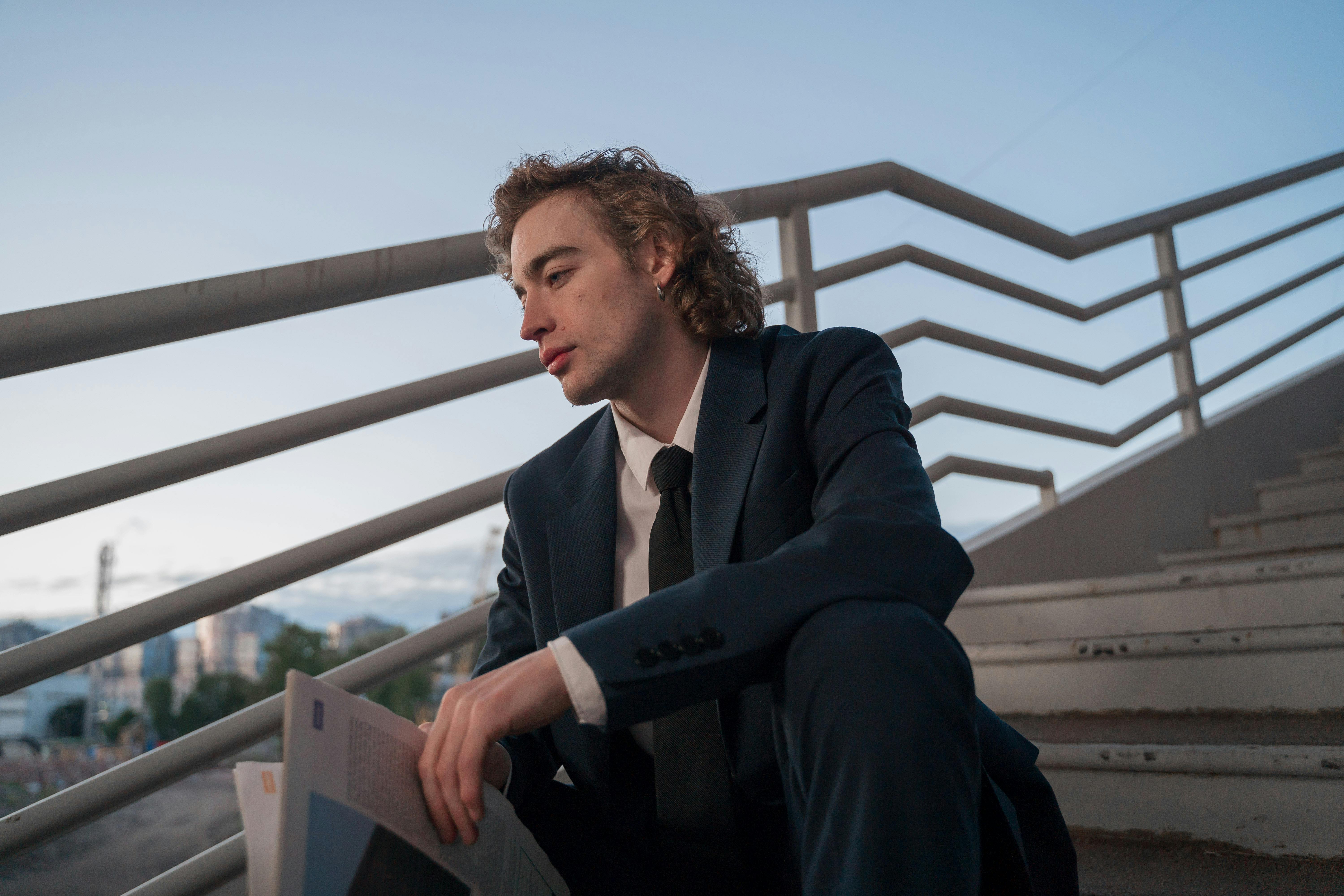 A person in a suit sits on stairs holding a newspaper.