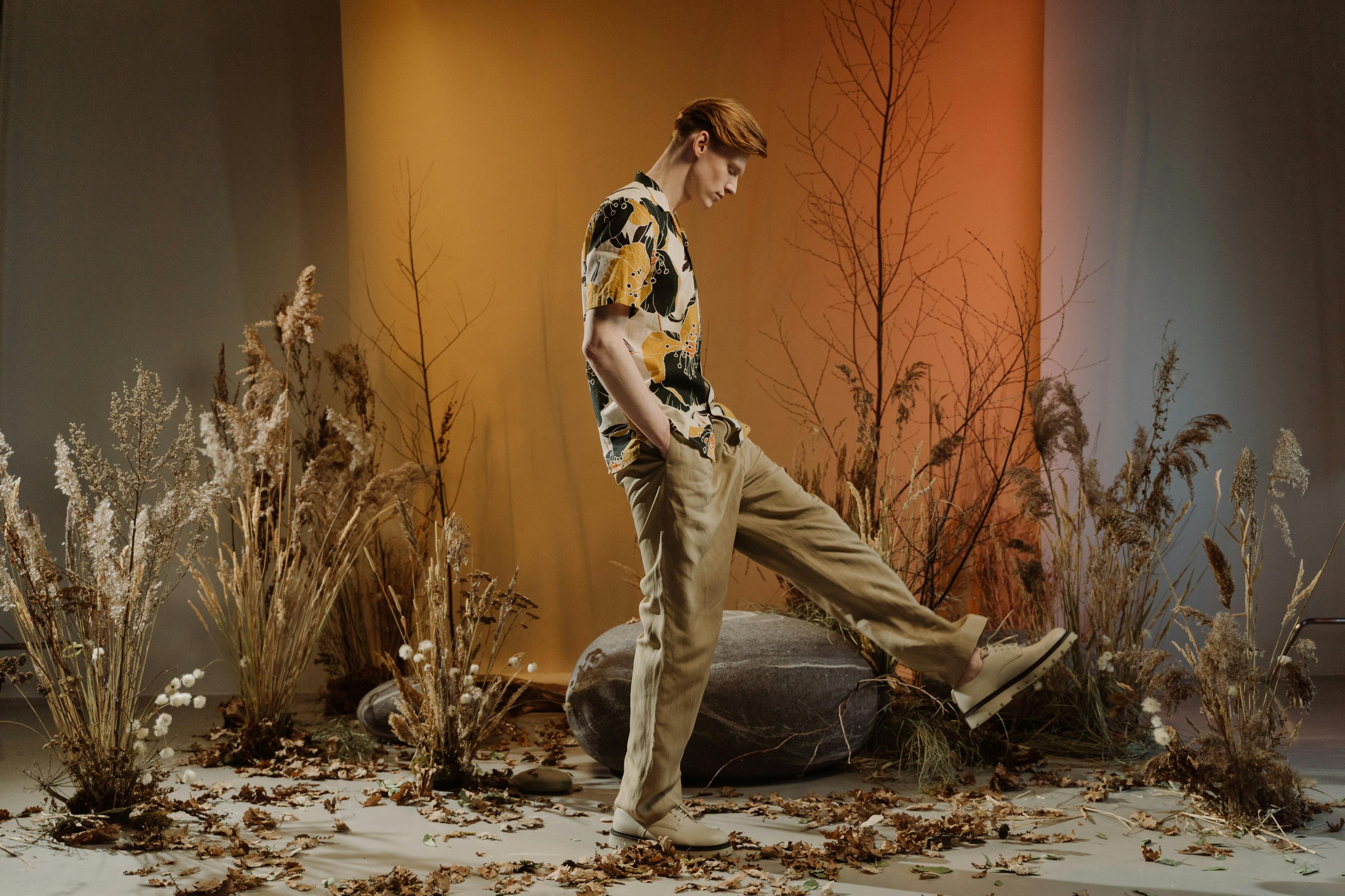 Person standing among dry plants, autumn leaves, and warm lighting.