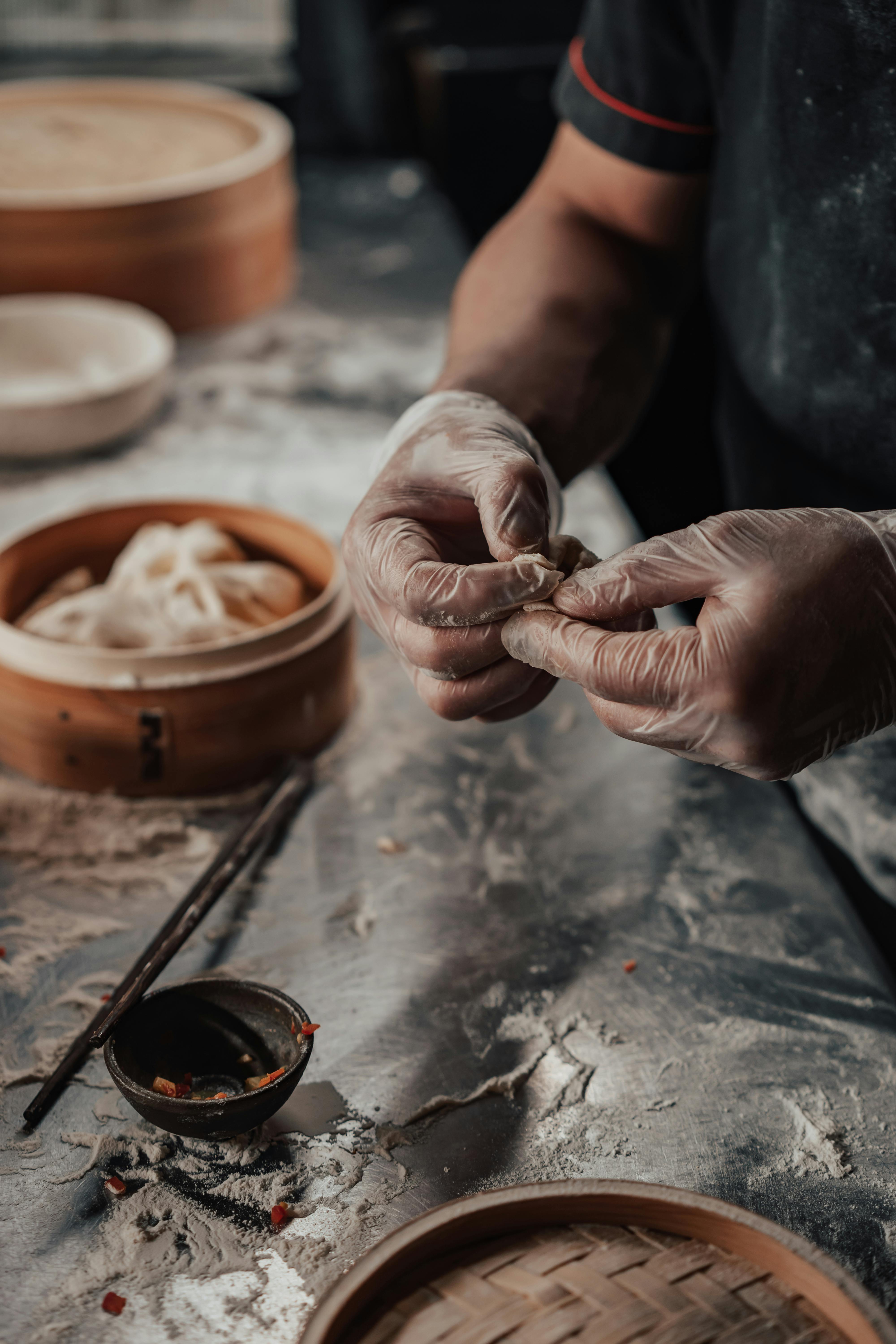 Person wearing gloves making dumplings on a floured surface.