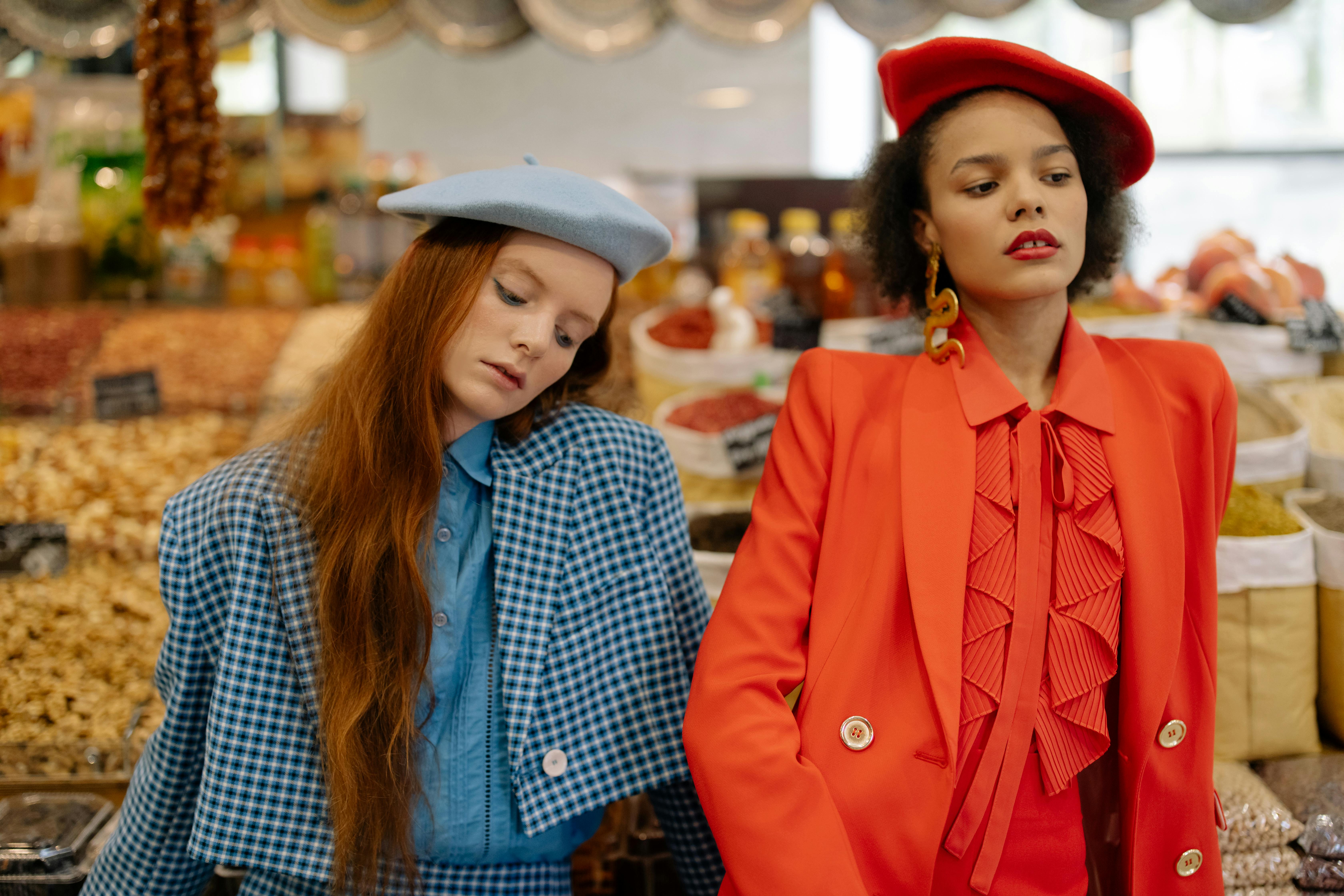 Two stylish people in a market with colorful spices and nuts.
