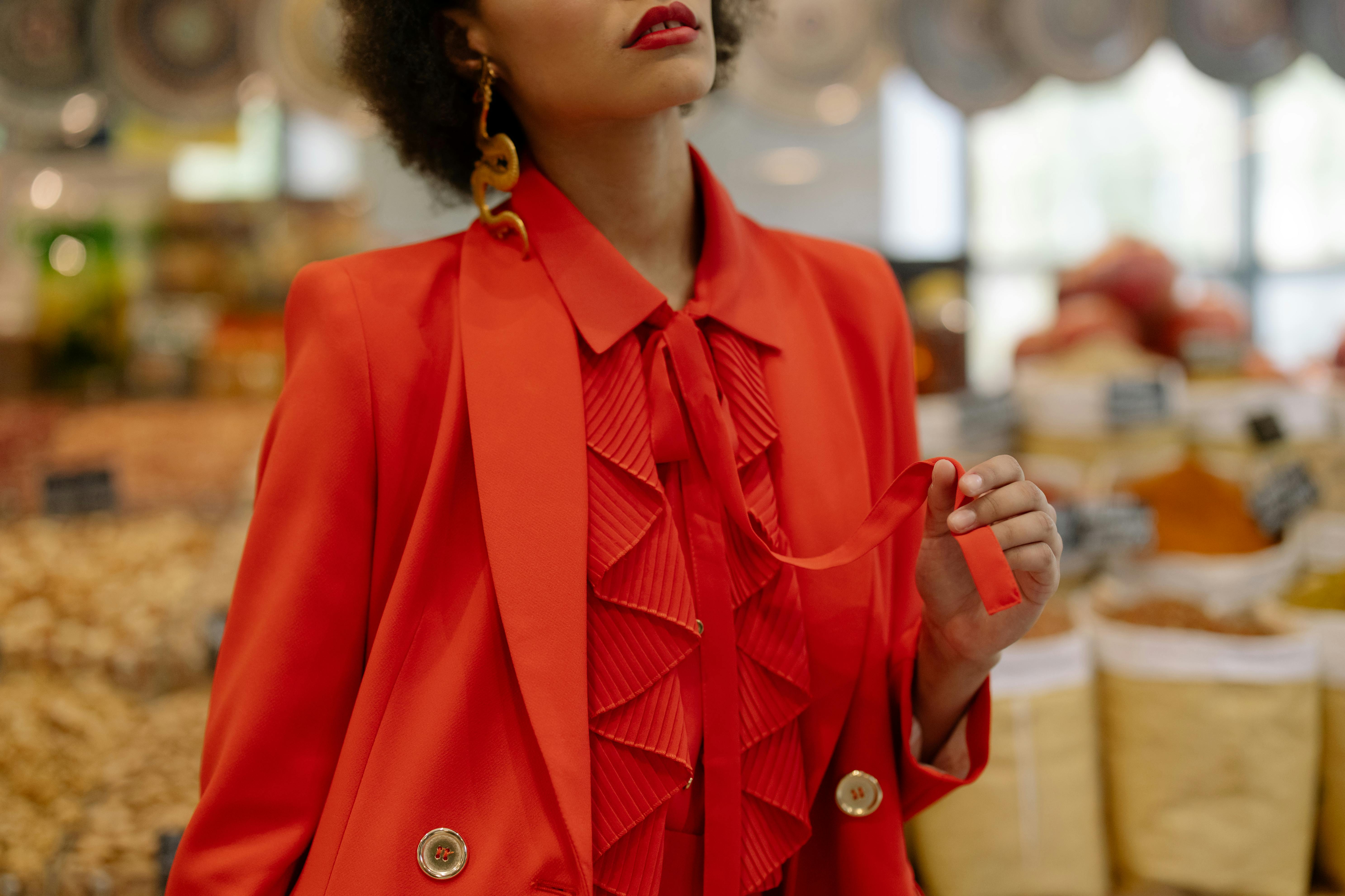A person in a red blazer and ruffled shirt holds a red ribbon.