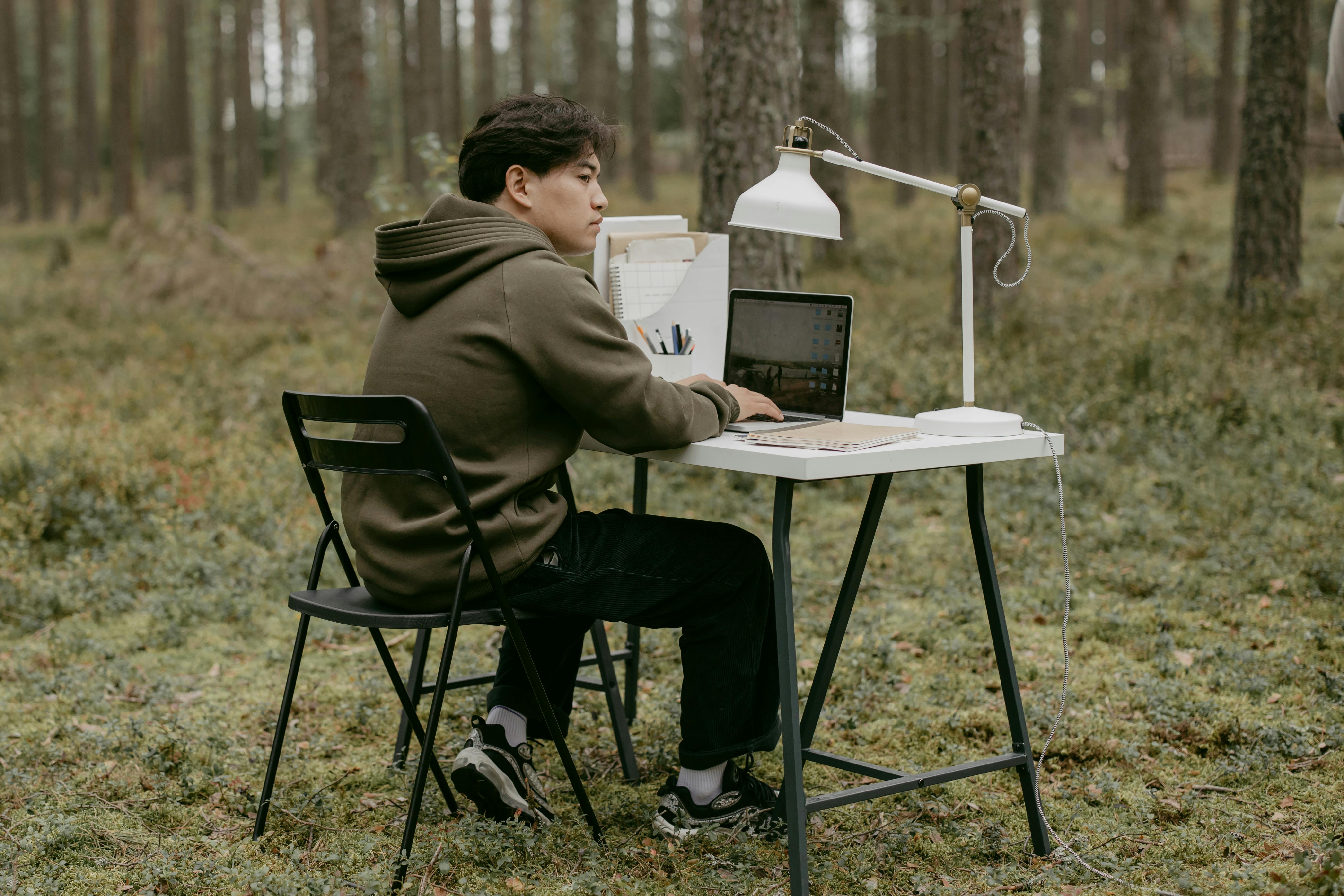 Person working on laptop at desk in forest setting.