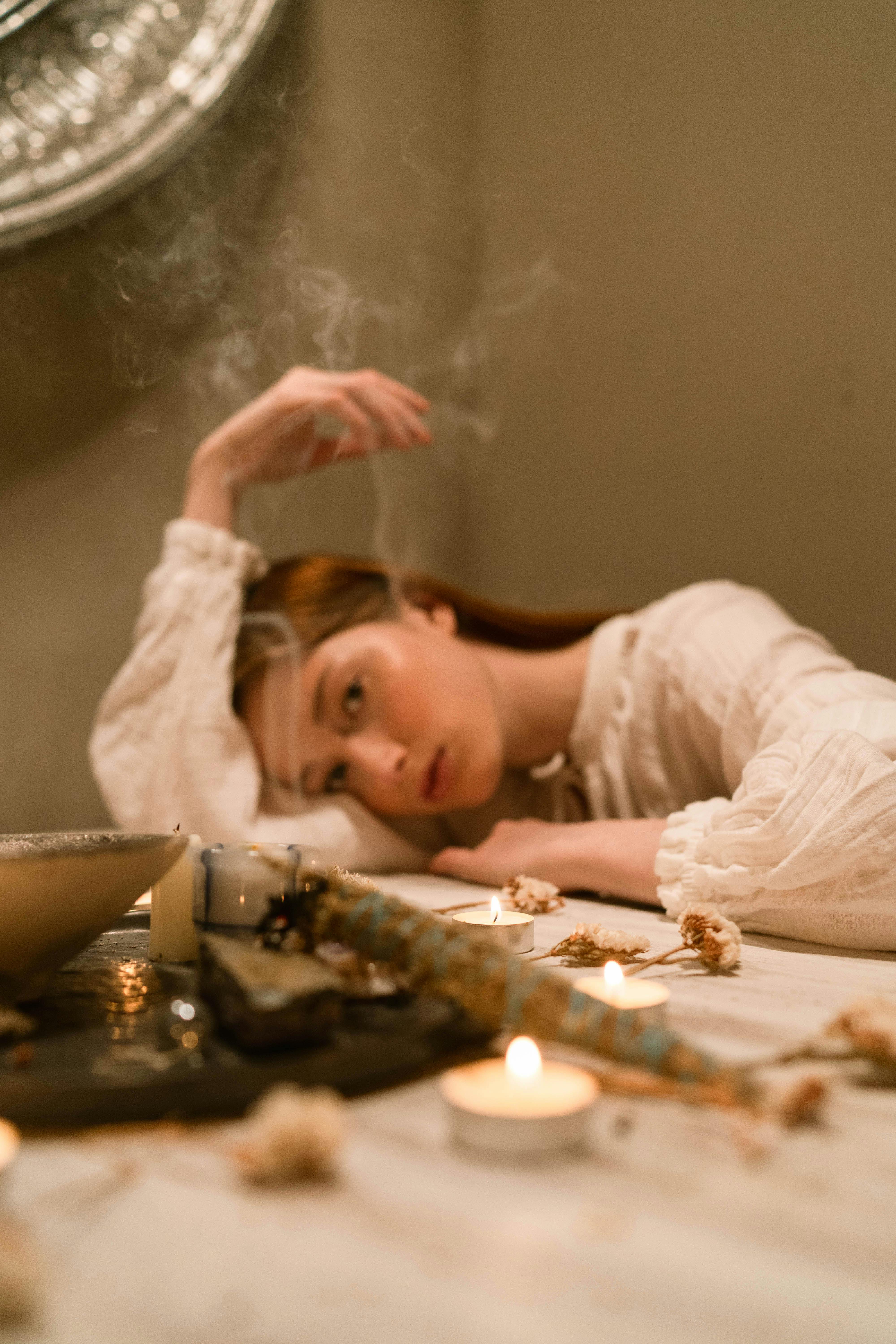 Person resting head on table with candles and dried flowers.