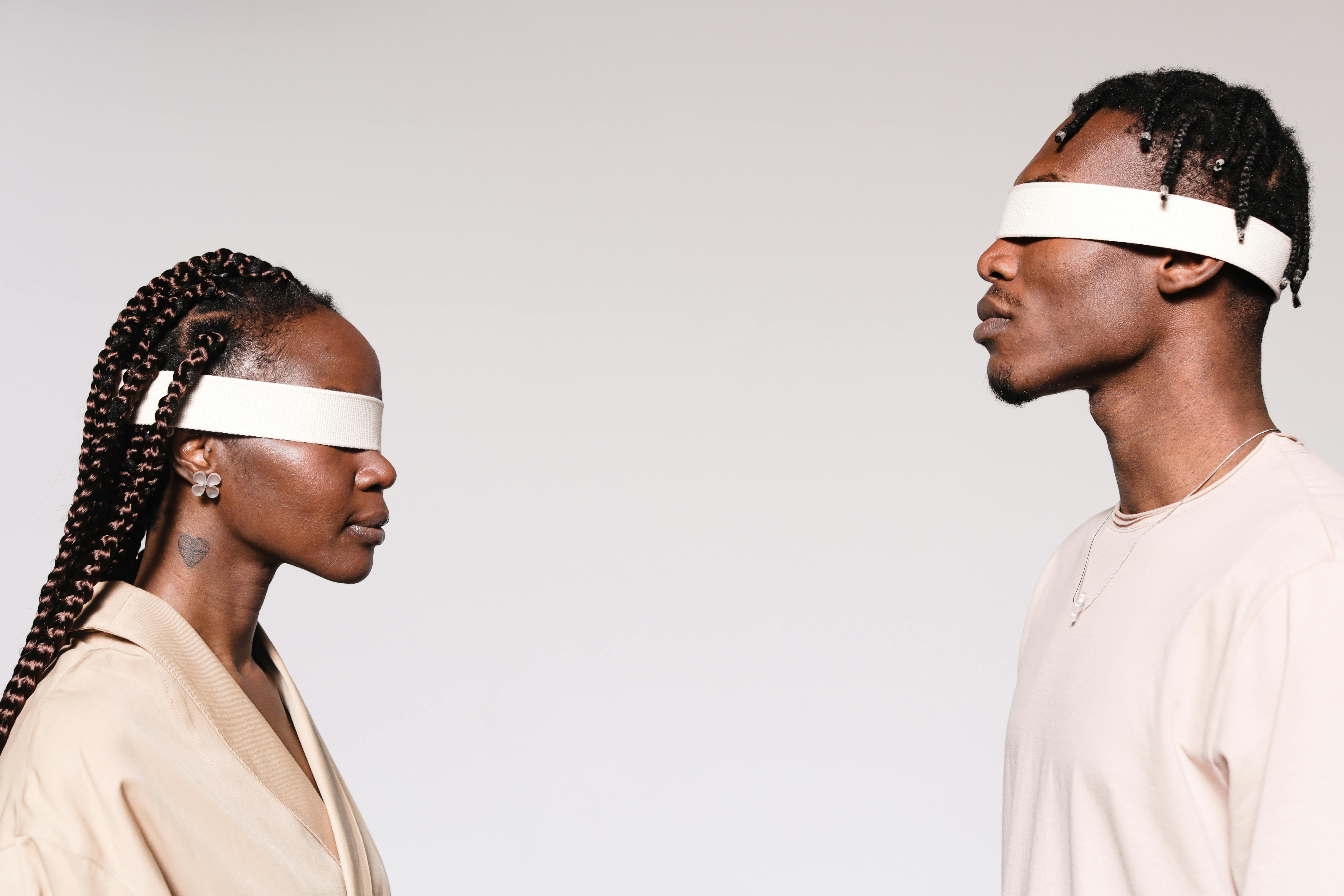 Two people facing each other, both wearing white blindfolds.