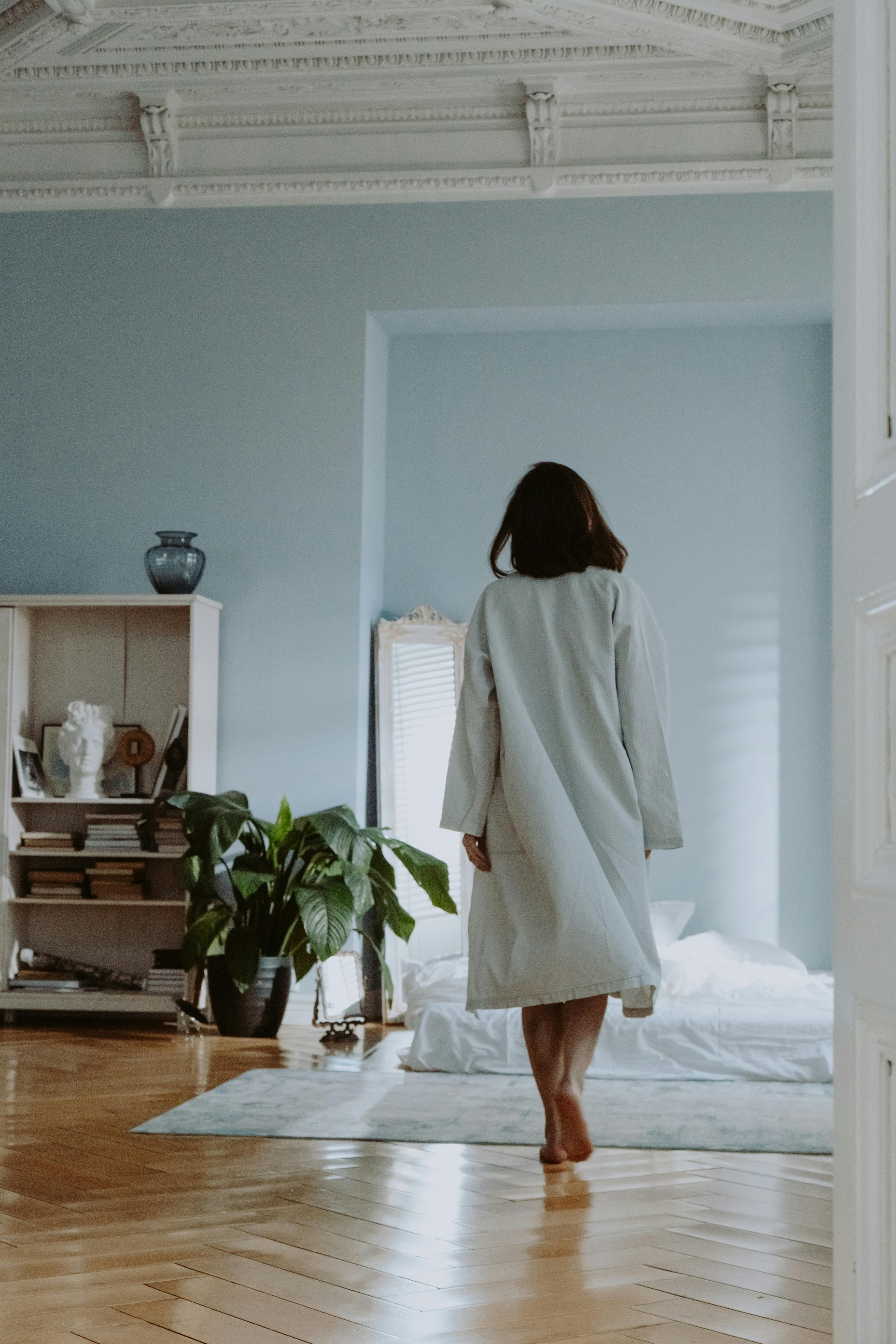 Person in robe walking in elegant, serene, light blue bedroom.