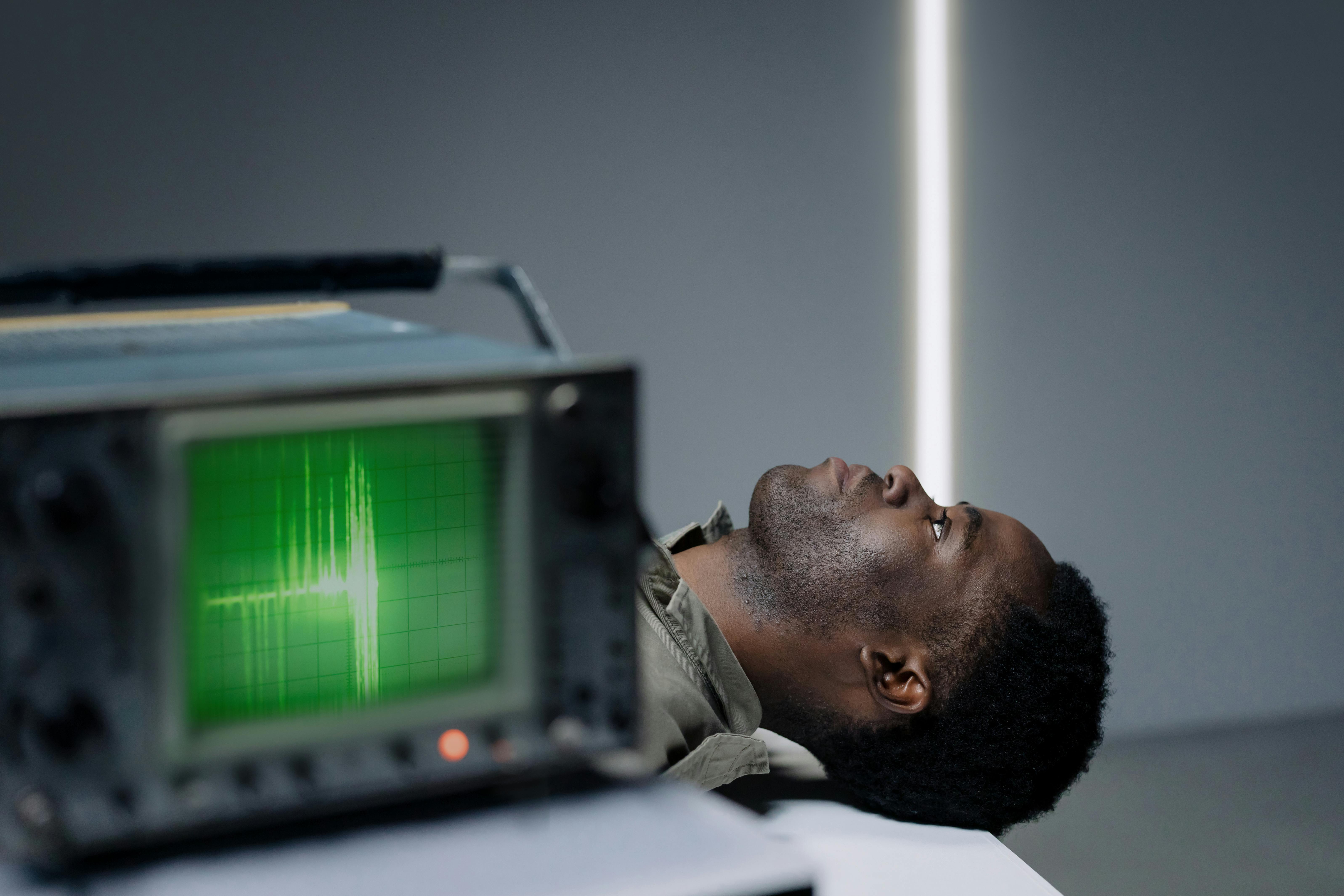 Person lying on table beside machine with green waveform display.