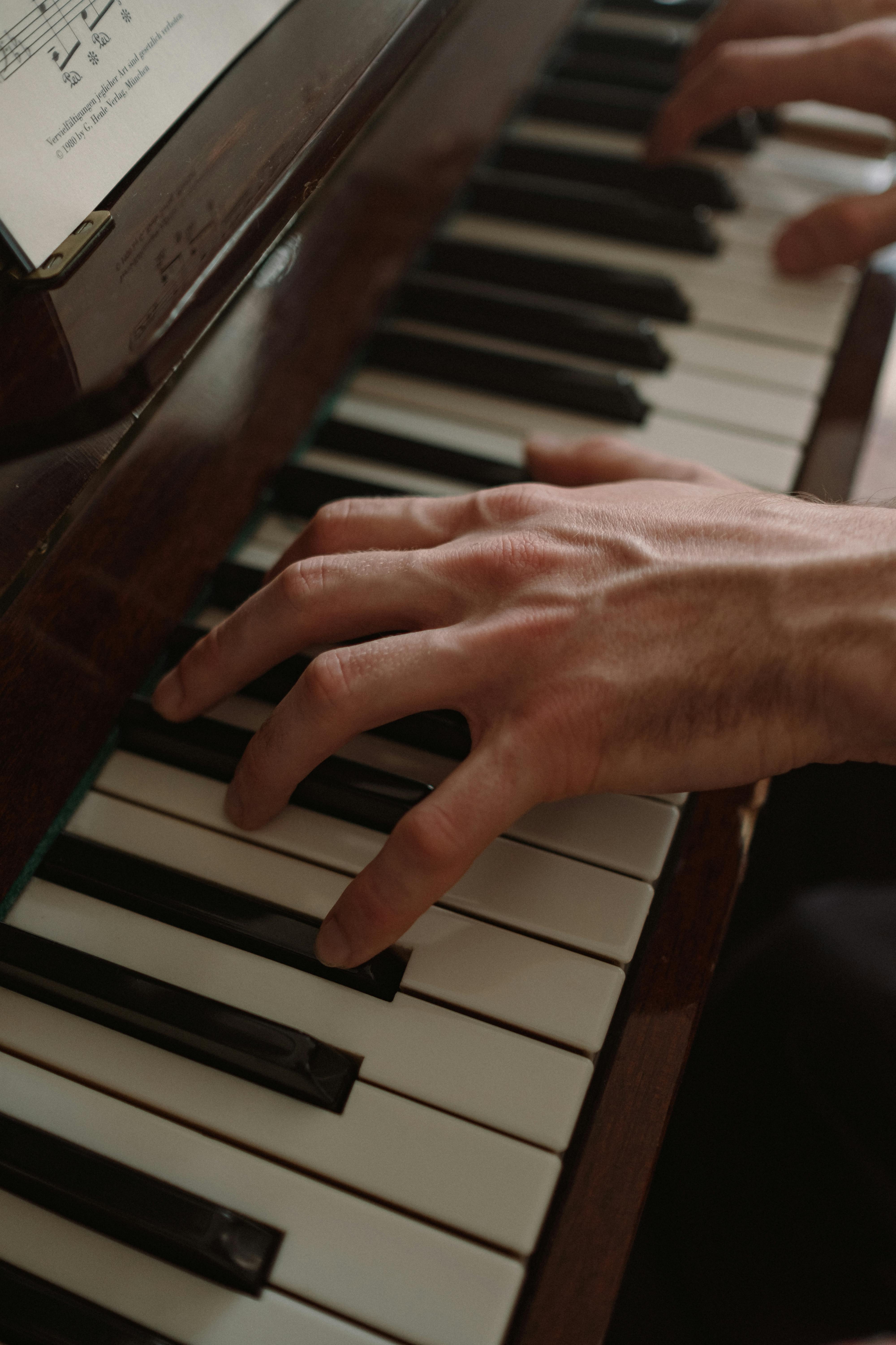 Hands playing piano keys with sheet music on display.