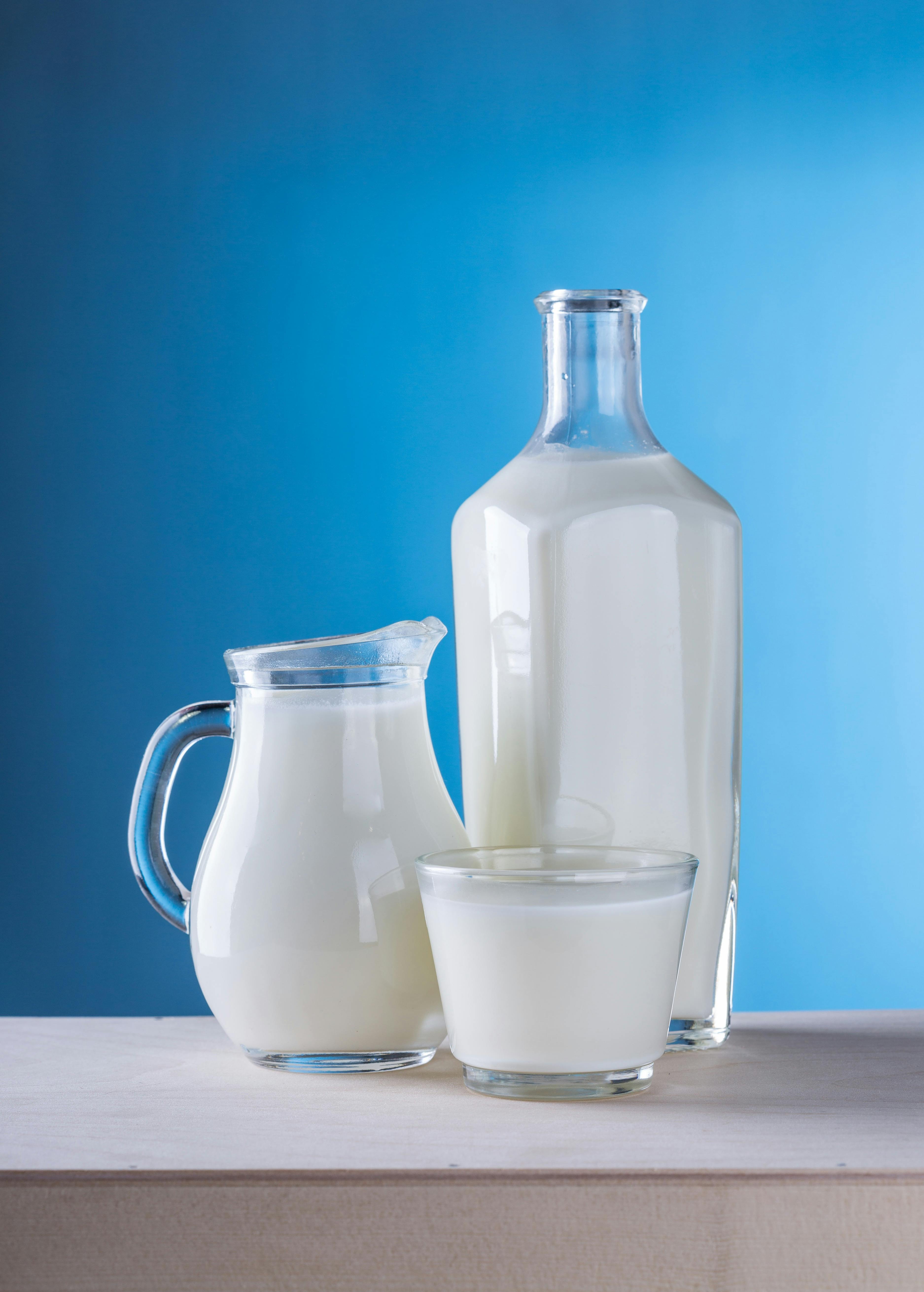 Glass bottle, jug, and cup filled with milk, blue background.