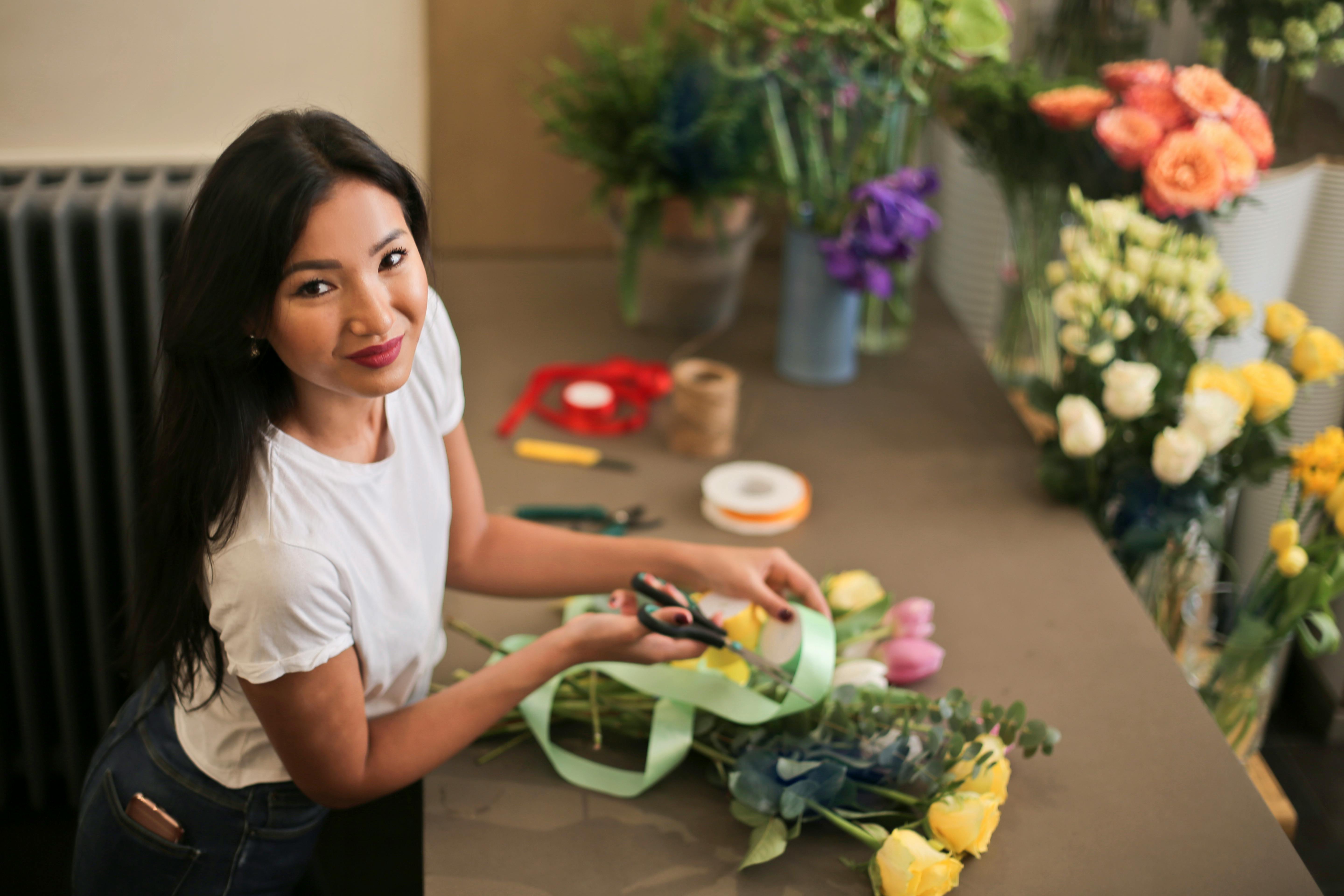 A person arranging flowers with ribbon and scissors.