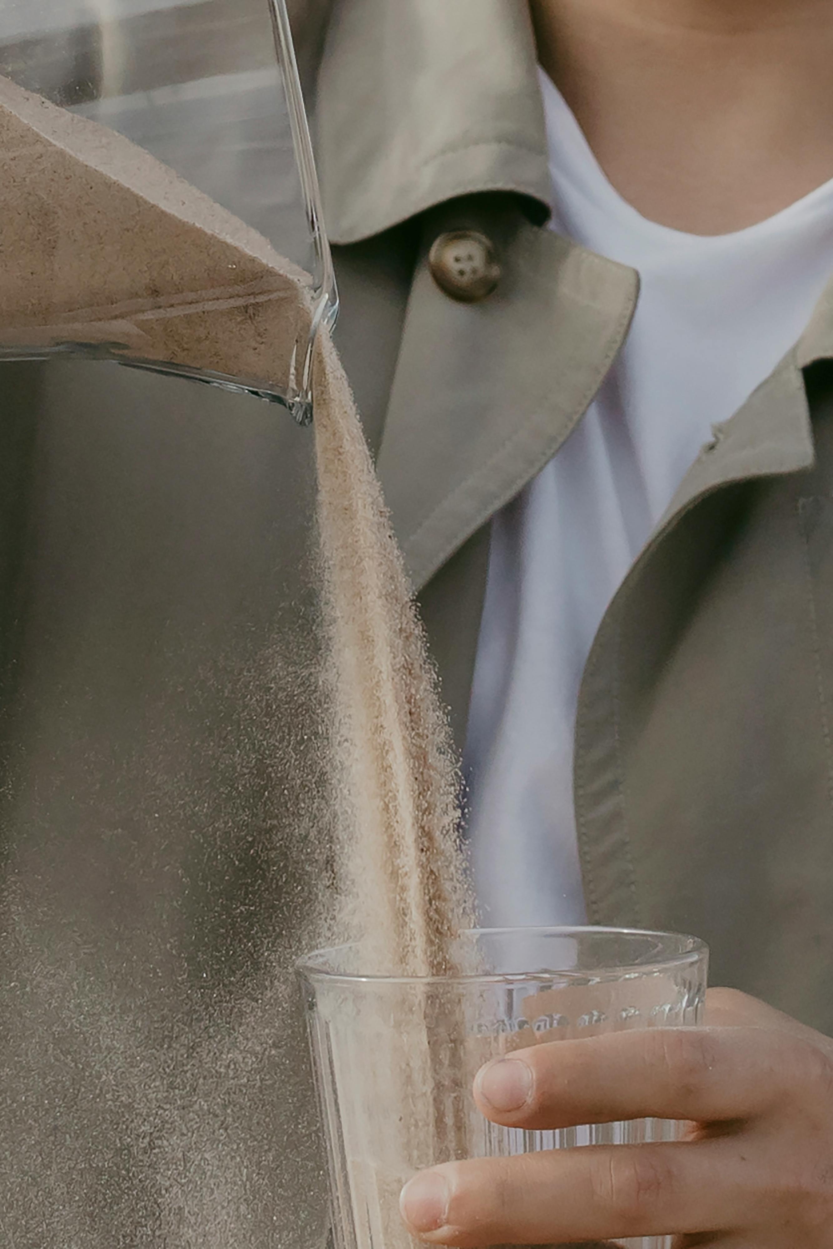 Powder being poured from container into glass held by person.
