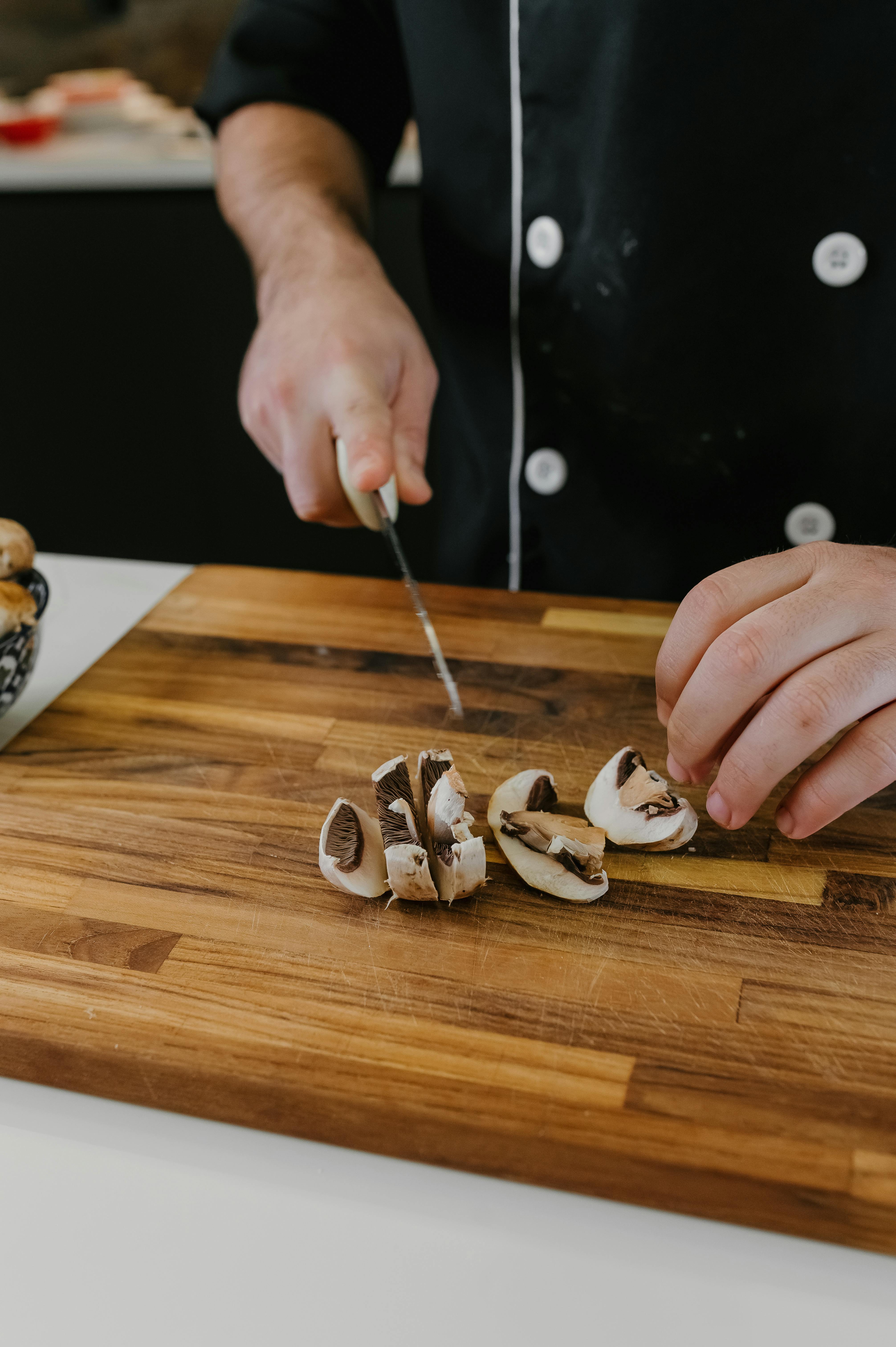 Person slicing mushrooms on a wooden cutting board in kitchen.
