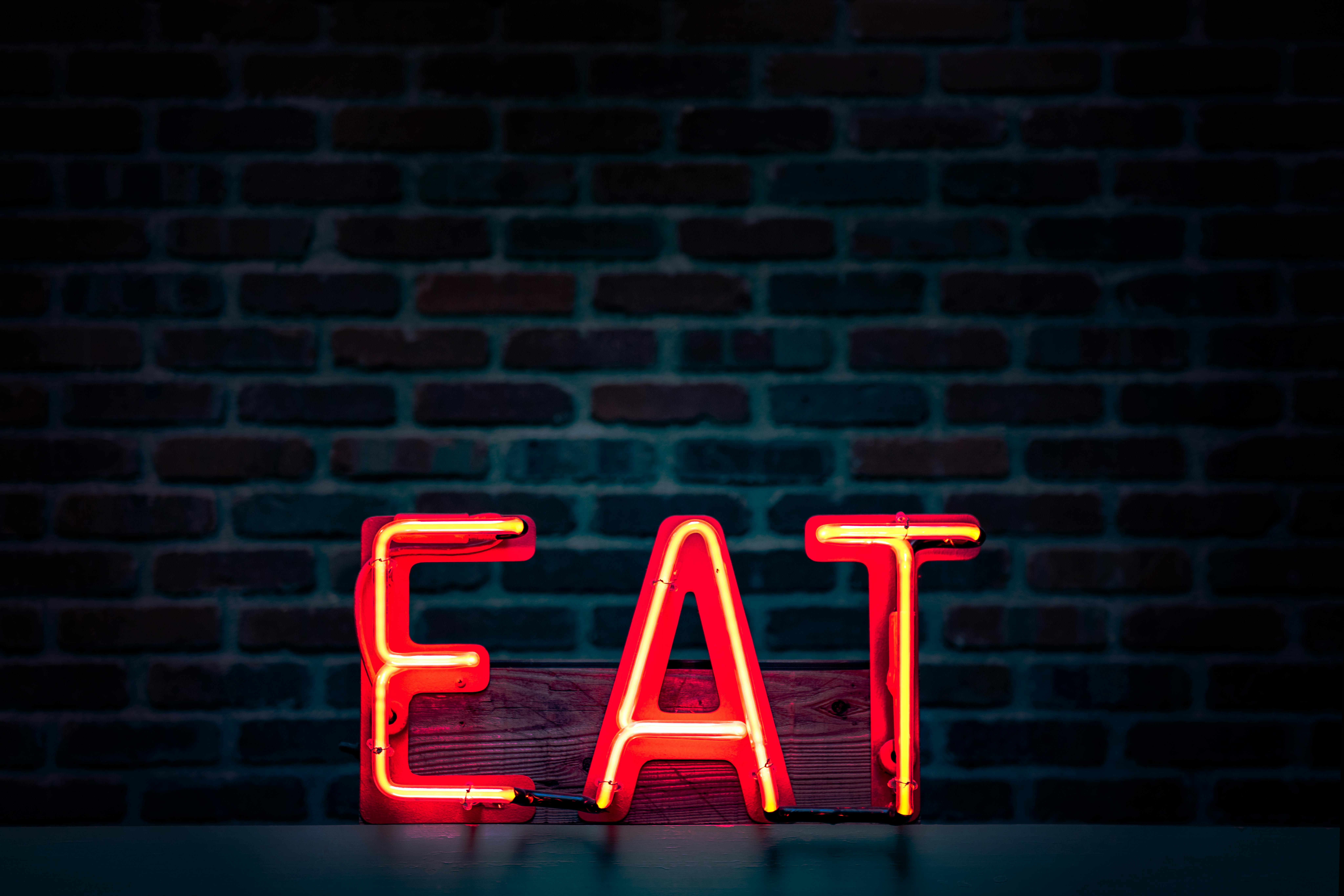 Neon sign spelling 'EAT' against a dark brick wall.