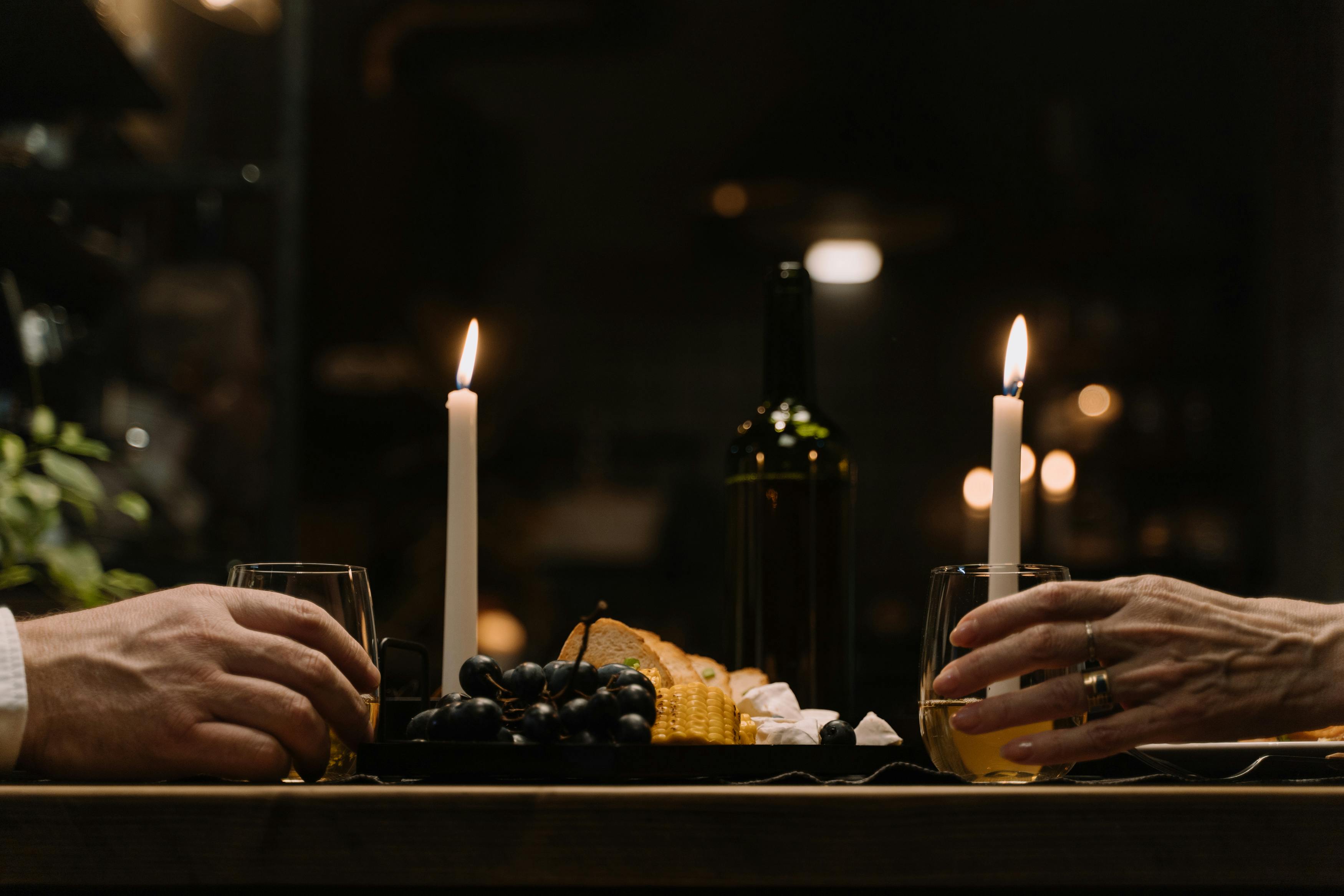 Candlelit dinner with wine, grapes, bread, and two people.