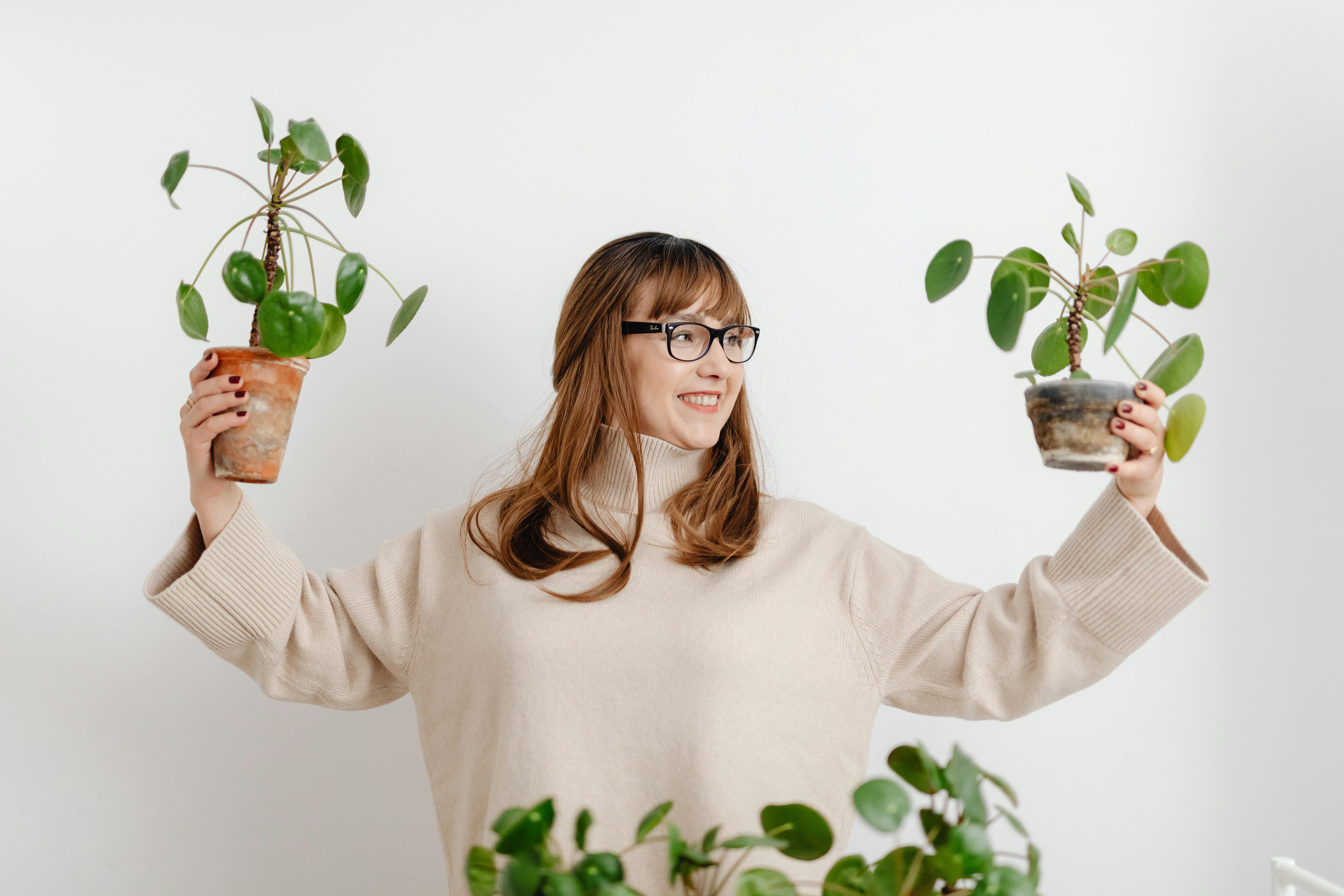 A person holds two potted plants against a white background.