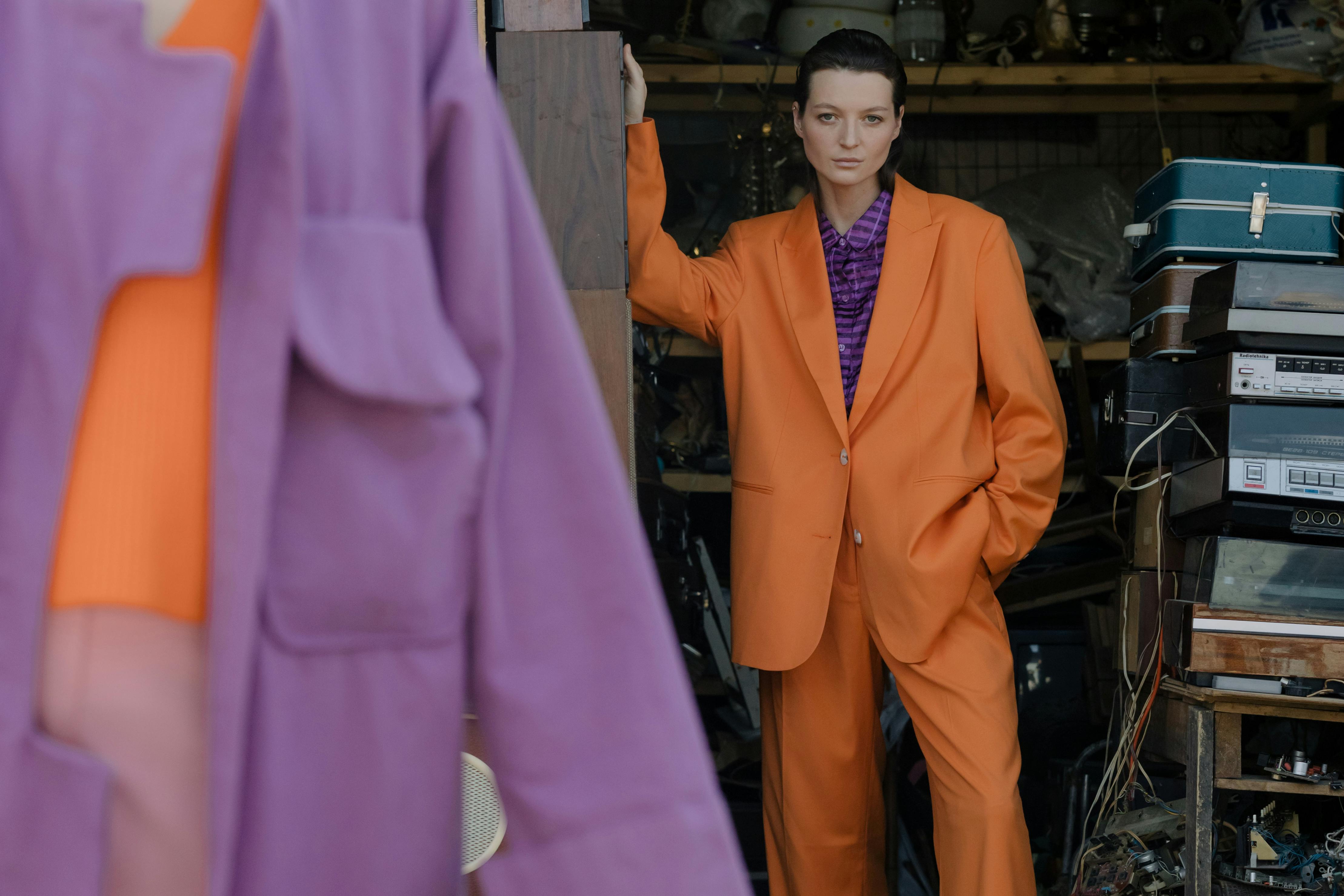 Person in orange suit stands near stacked electronics and luggage.