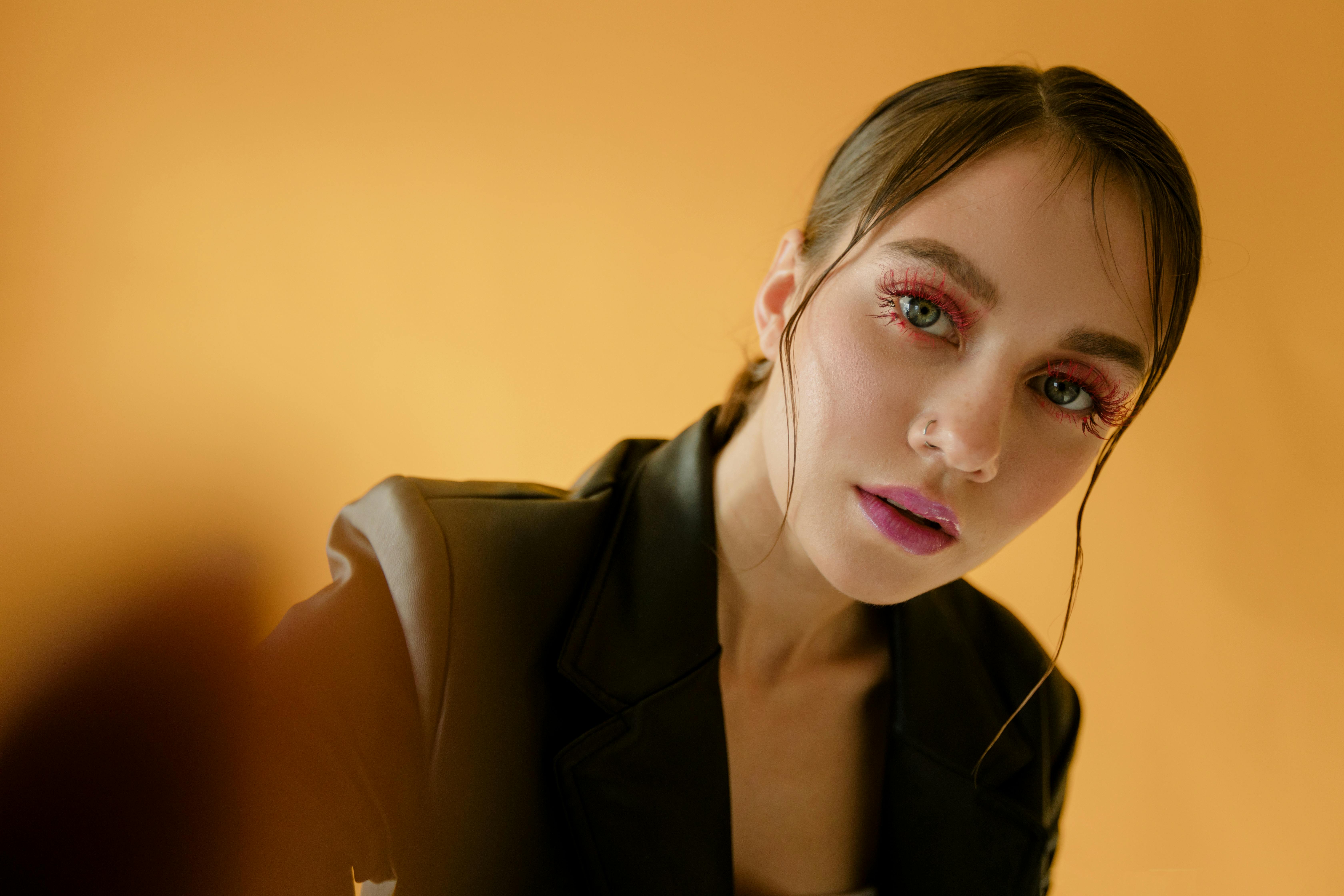 Person with dramatic makeup and black jacket against orange background.