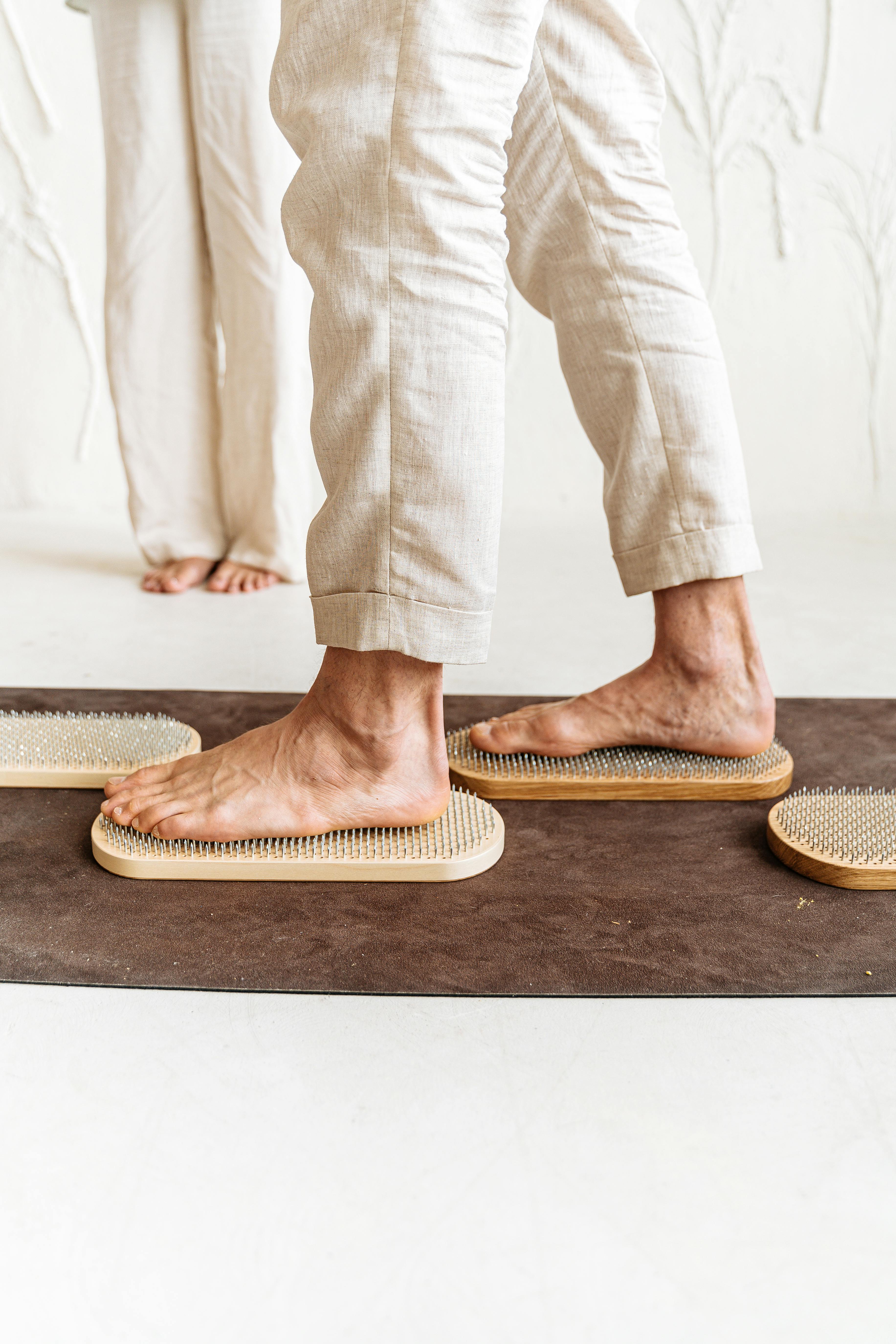 Person standing on wooden boards with metal spikes, barefoot indoors.