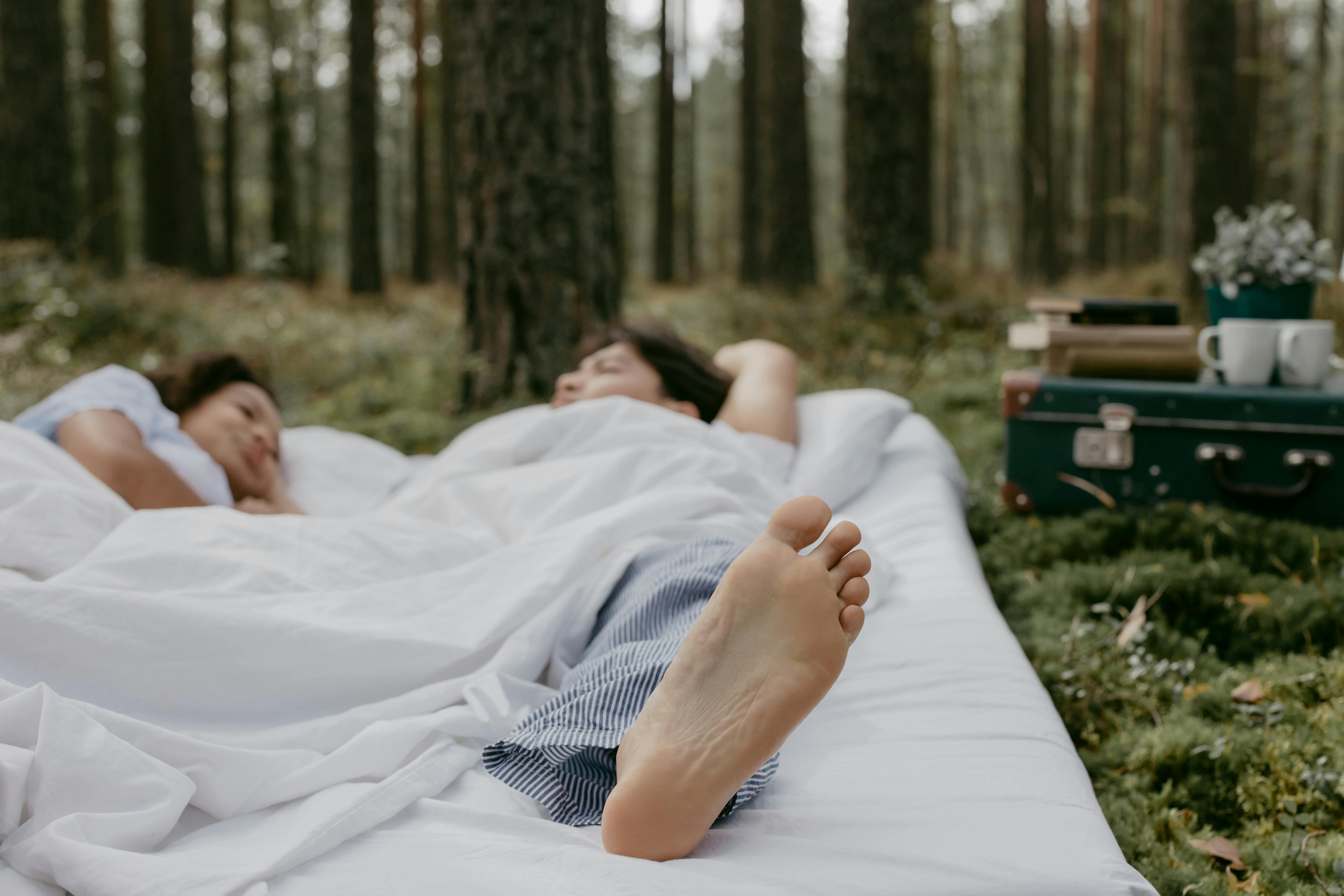 Two people relaxing on a bed outdoors in a forest.