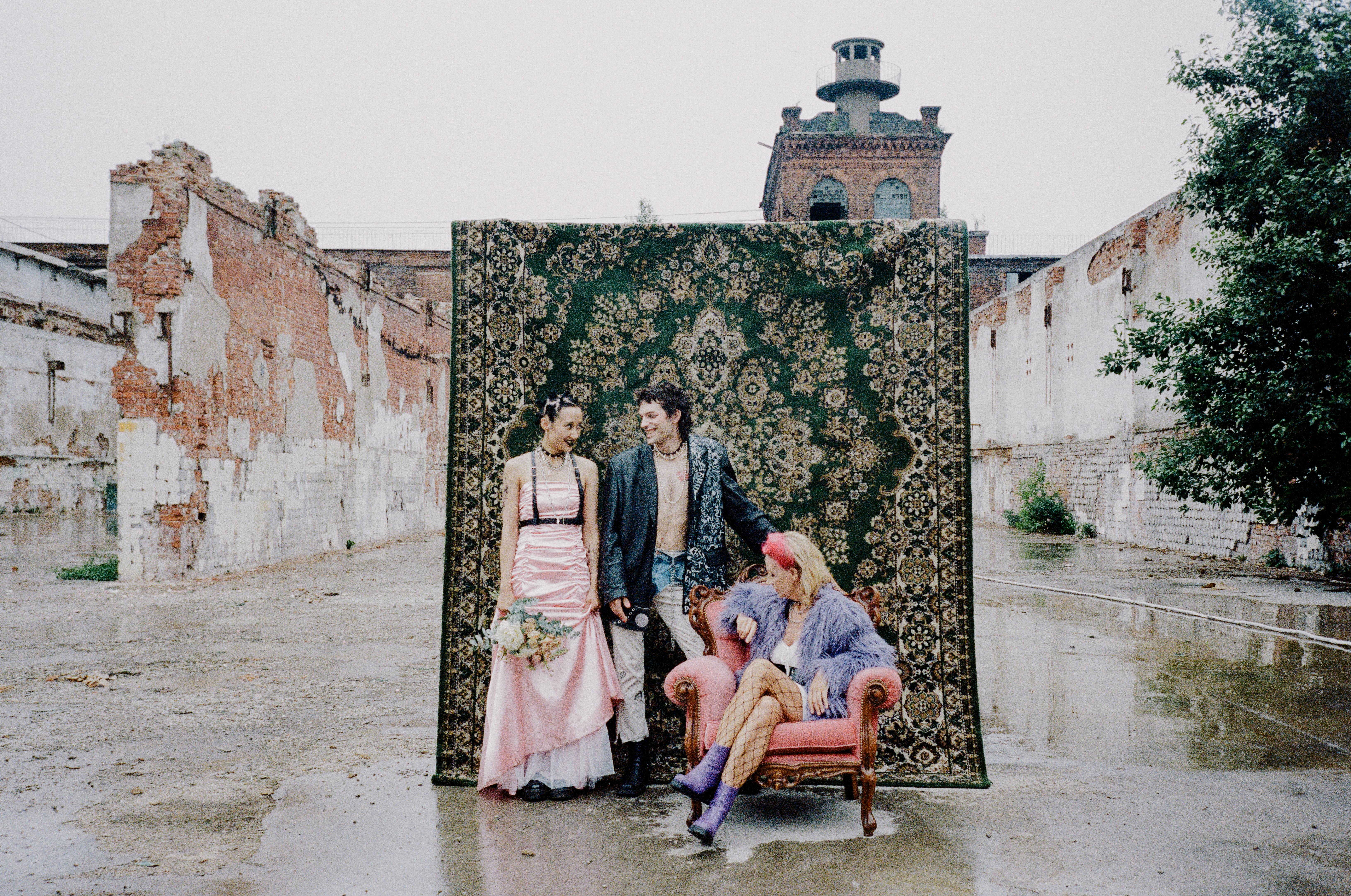 People posing in front of a rug in a ruined industrial setting.