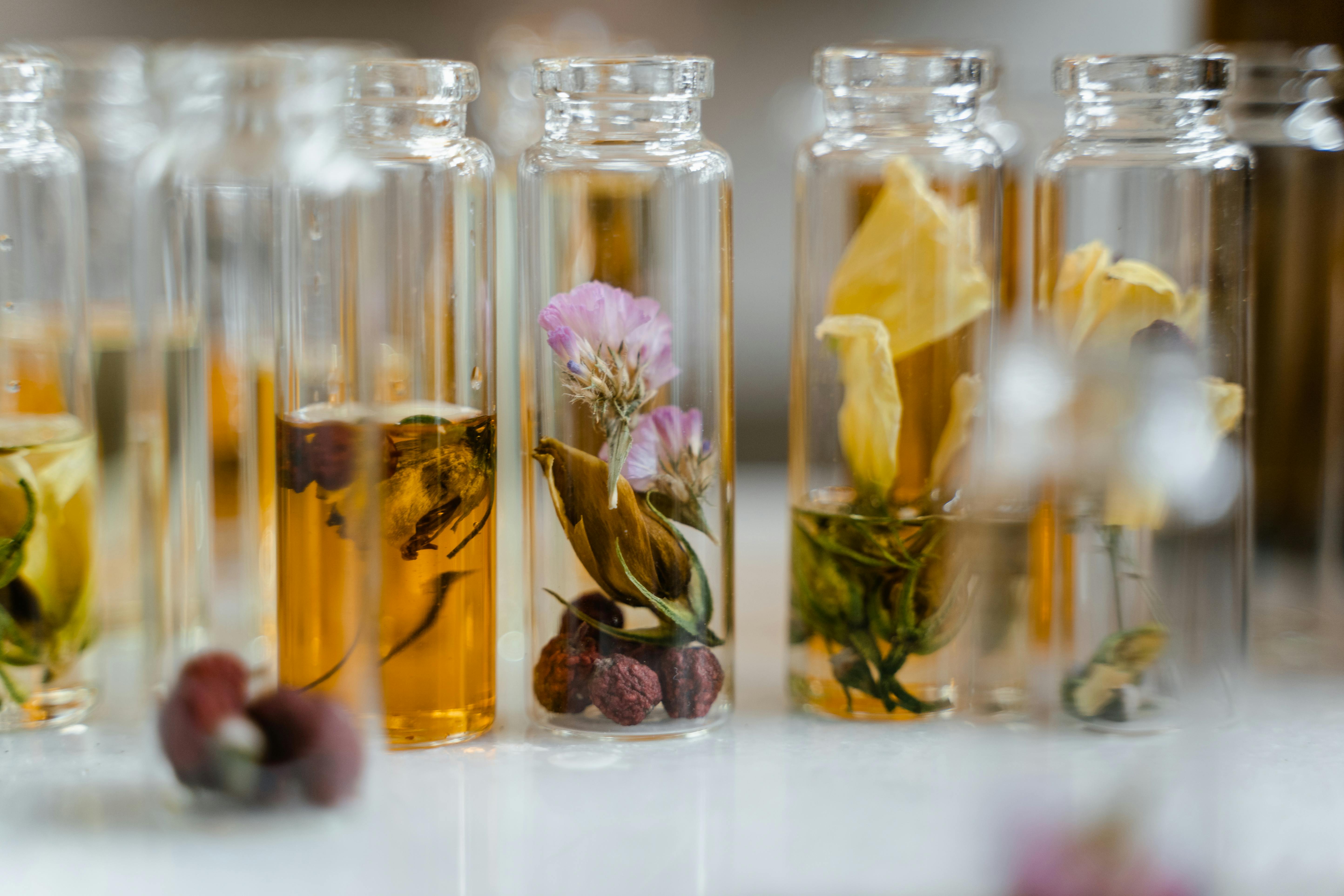 Glass vials filled with dried flowers and amber liquid, arranged closely.