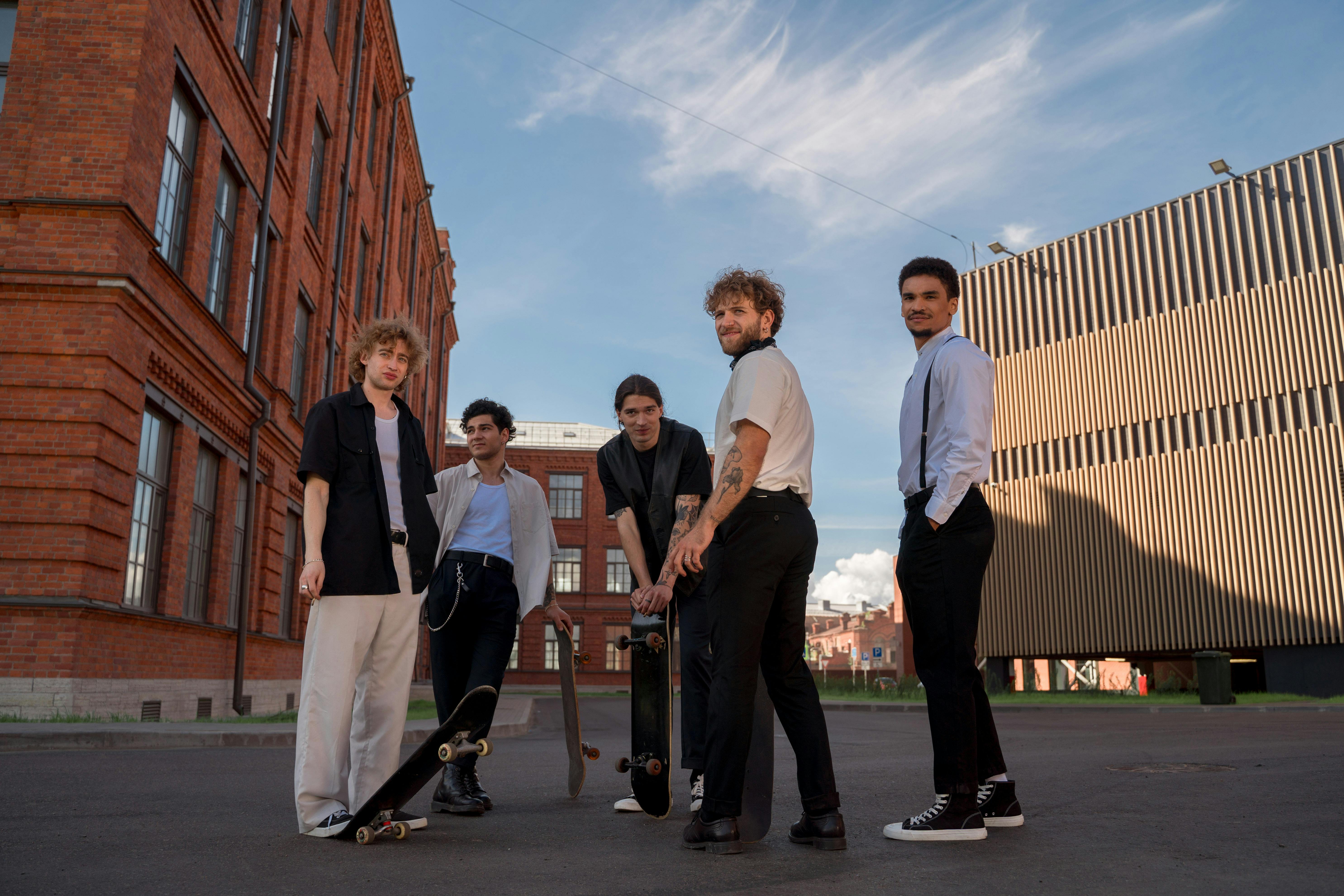 Four young men with skateboards stand outside buildings.