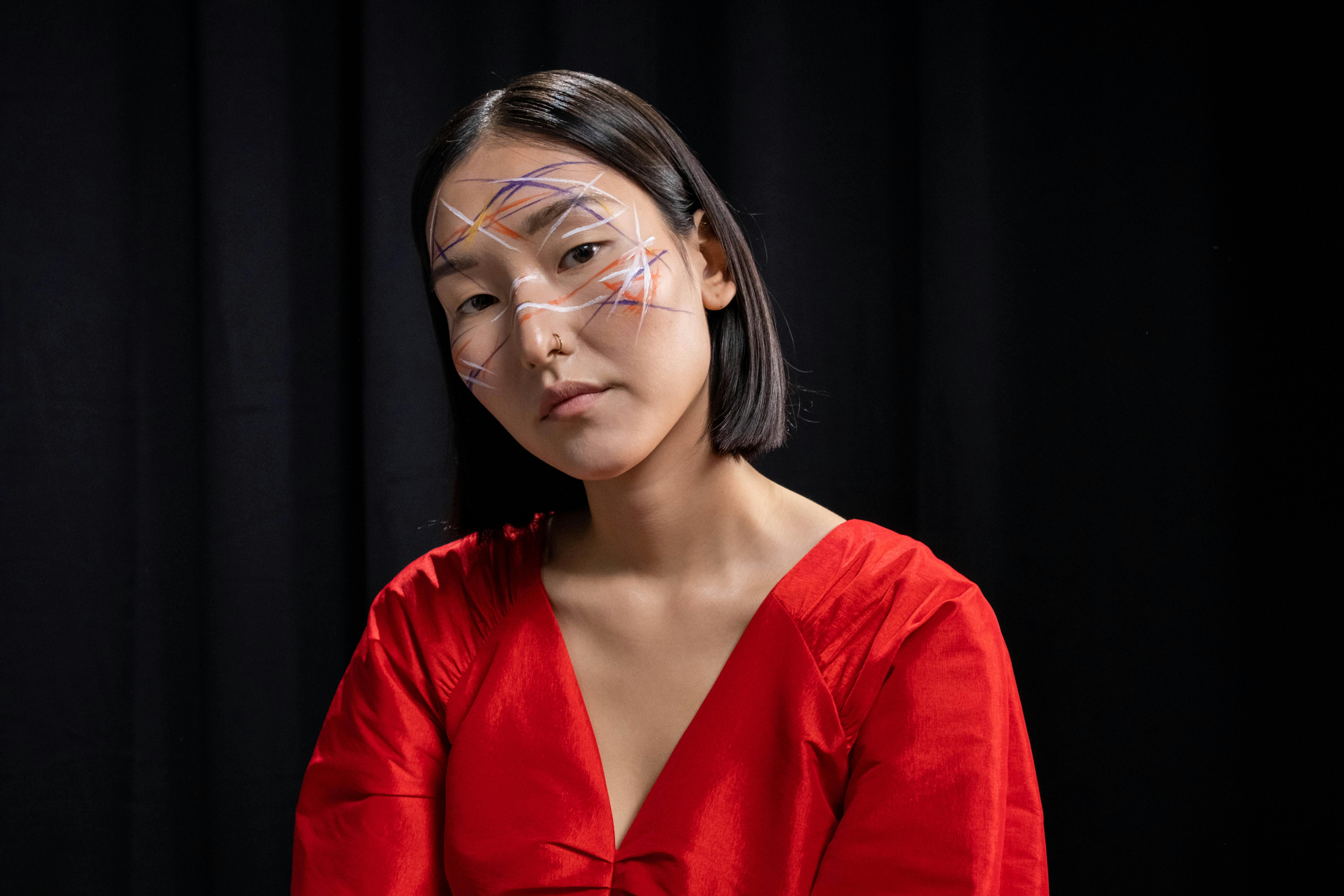 Person in red outfit with abstract face paint, black background.